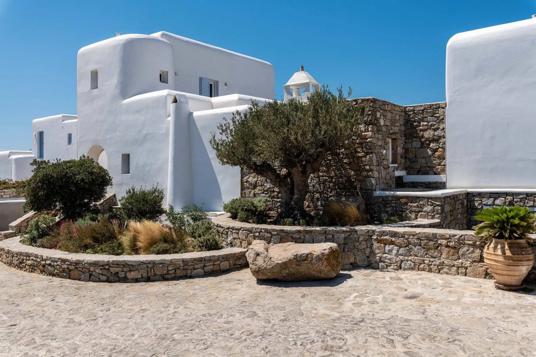 Whitewashed buildings frame a stone courtyard with a tree and raised stone steps.