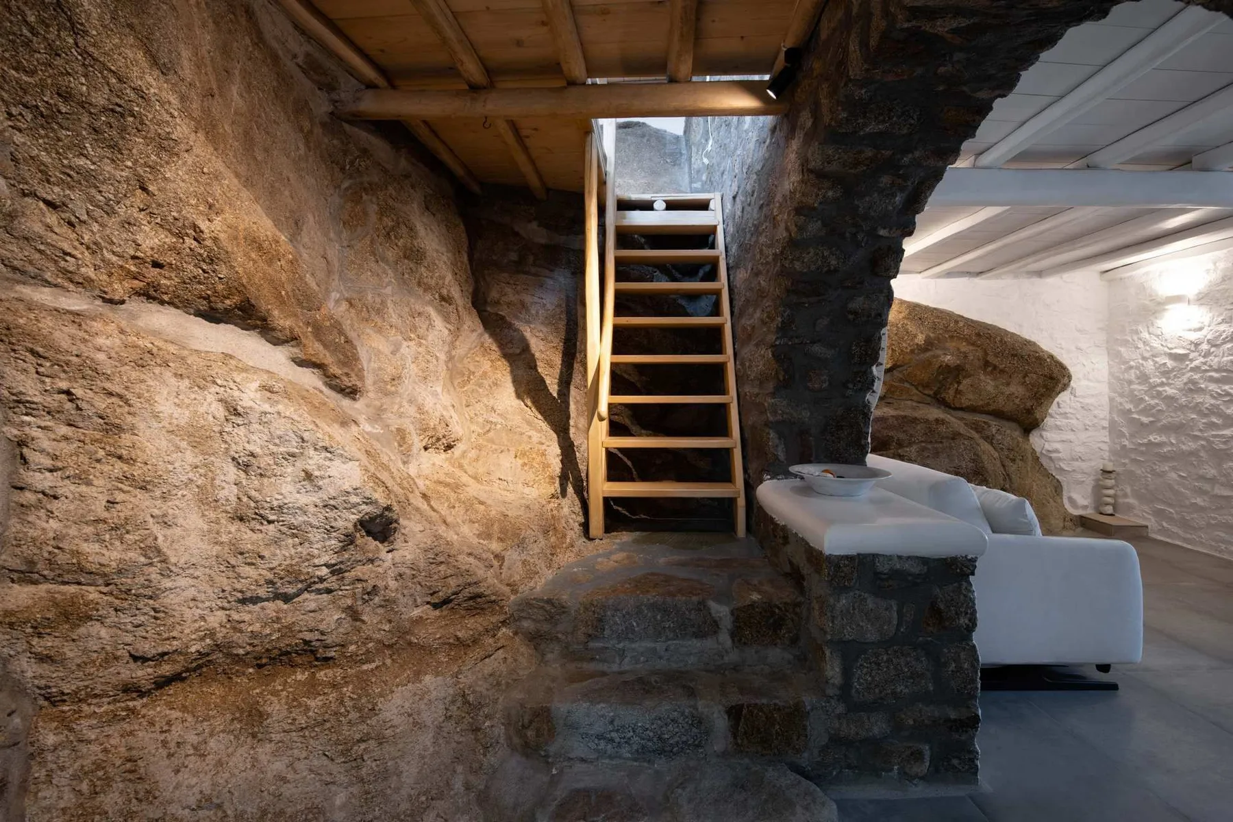 A stone interior with a wooden ladder beside a white seating area.
