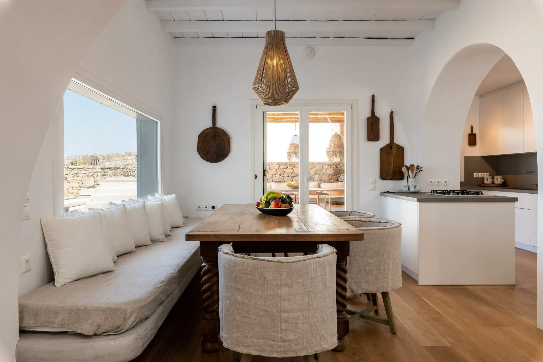 A bright dining area with a wooden table, built-in seating, and an adjoining kitchen.