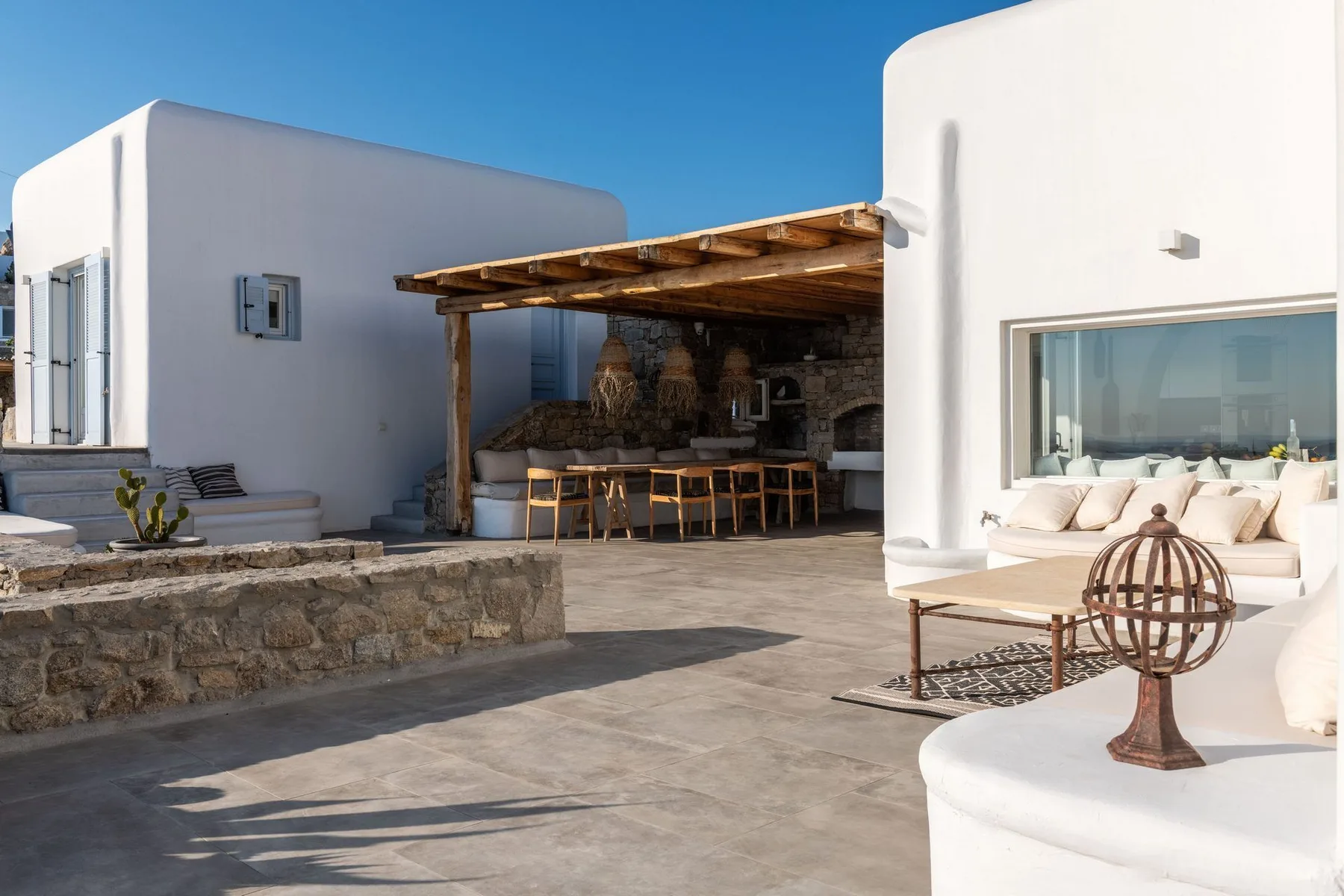 A sunny outdoor patio has white seating beside a covered bar area.