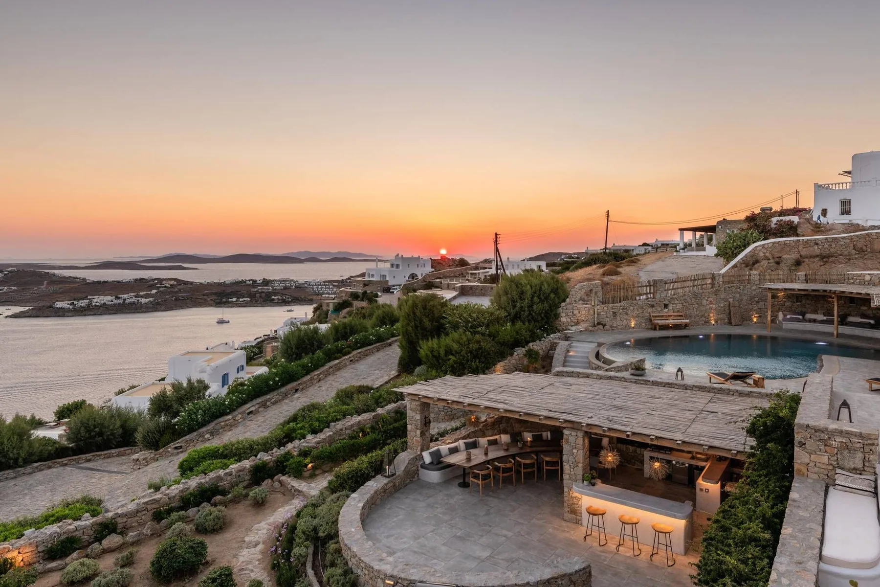 A seaside terrace overlooks a pool and the bay at sunset.