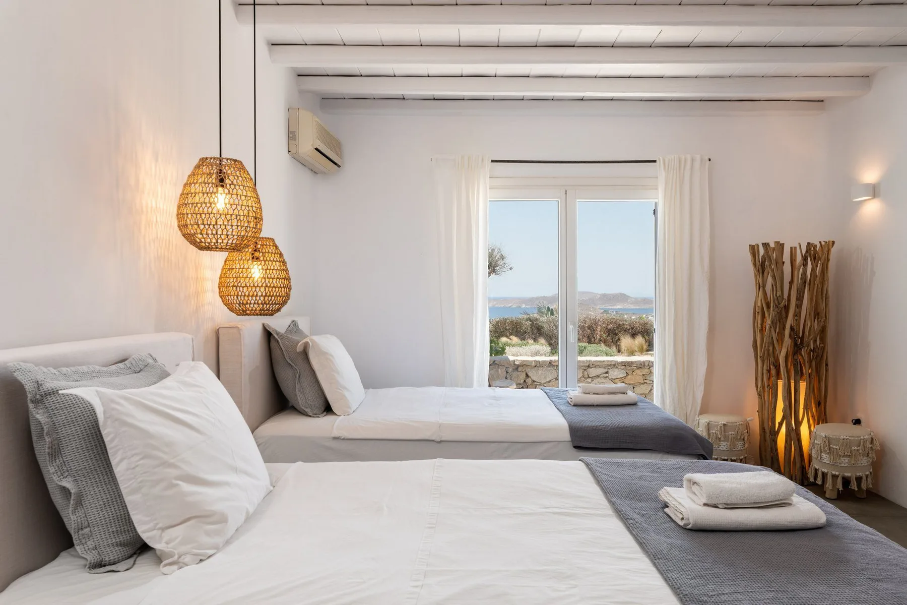 A bright bedroom with two beds and glass doors opening to a view.