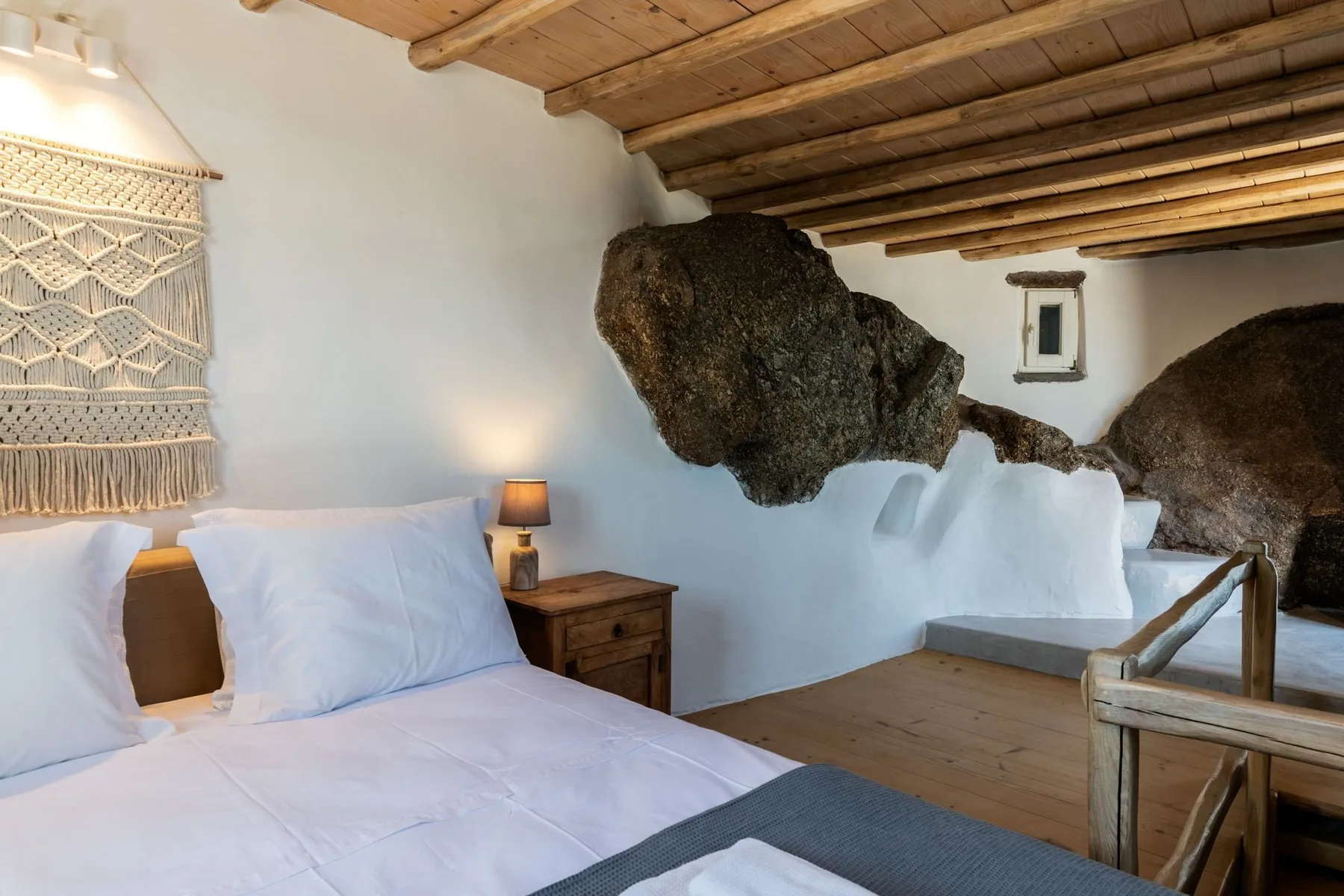 A bedroom with a bed, wooden ceiling, and exposed rock features in the walls.