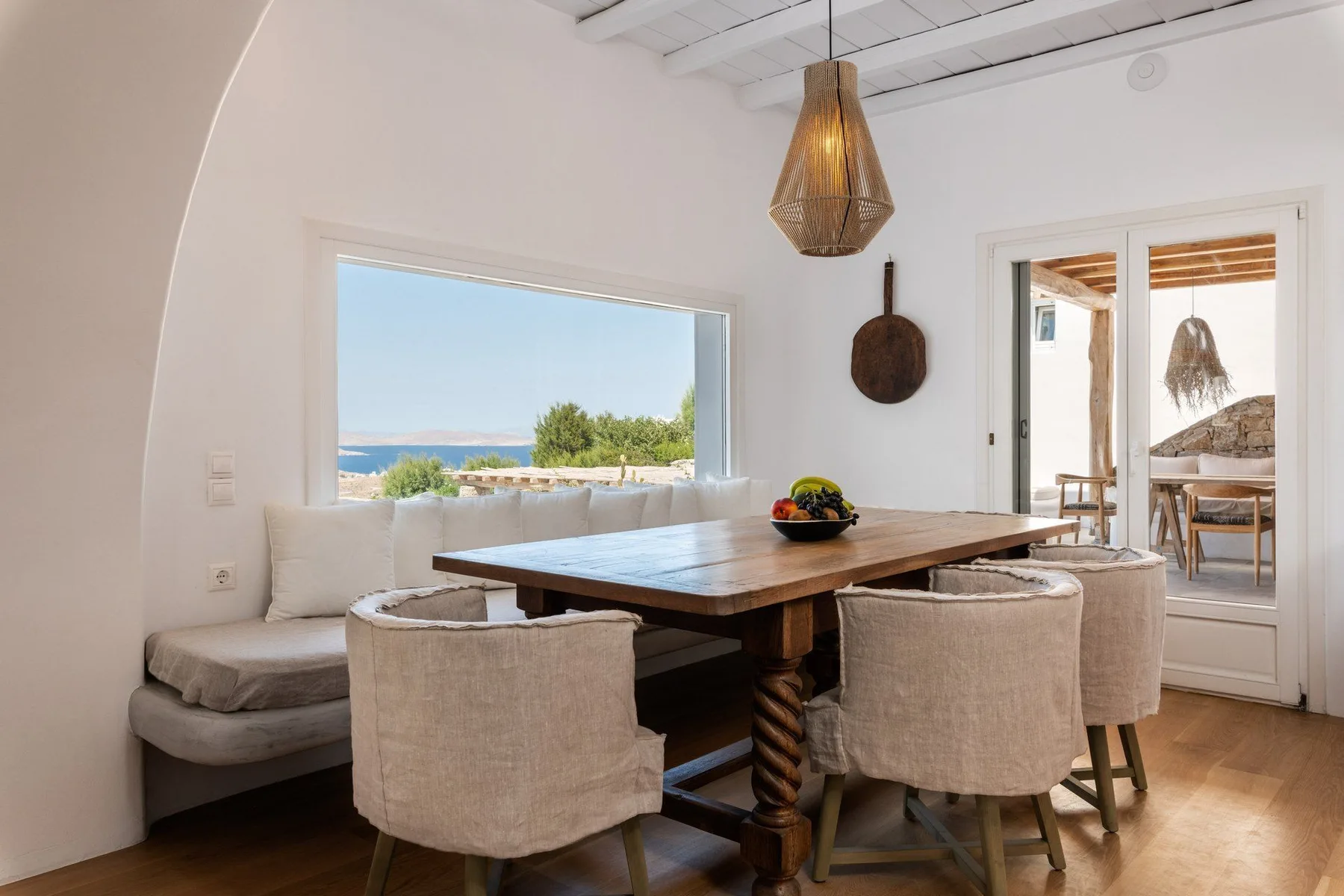 A dining area with a wooden table and cushioned seating beside a large window.