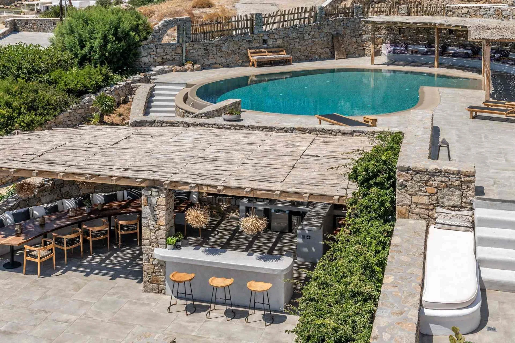 An outdoor pool and patio, with shaded seating beneath a wooden pergola.