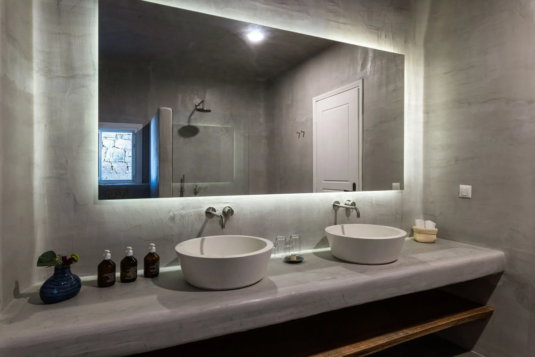 A bathroom vanity with two vessel sinks and a large illuminated mirror.