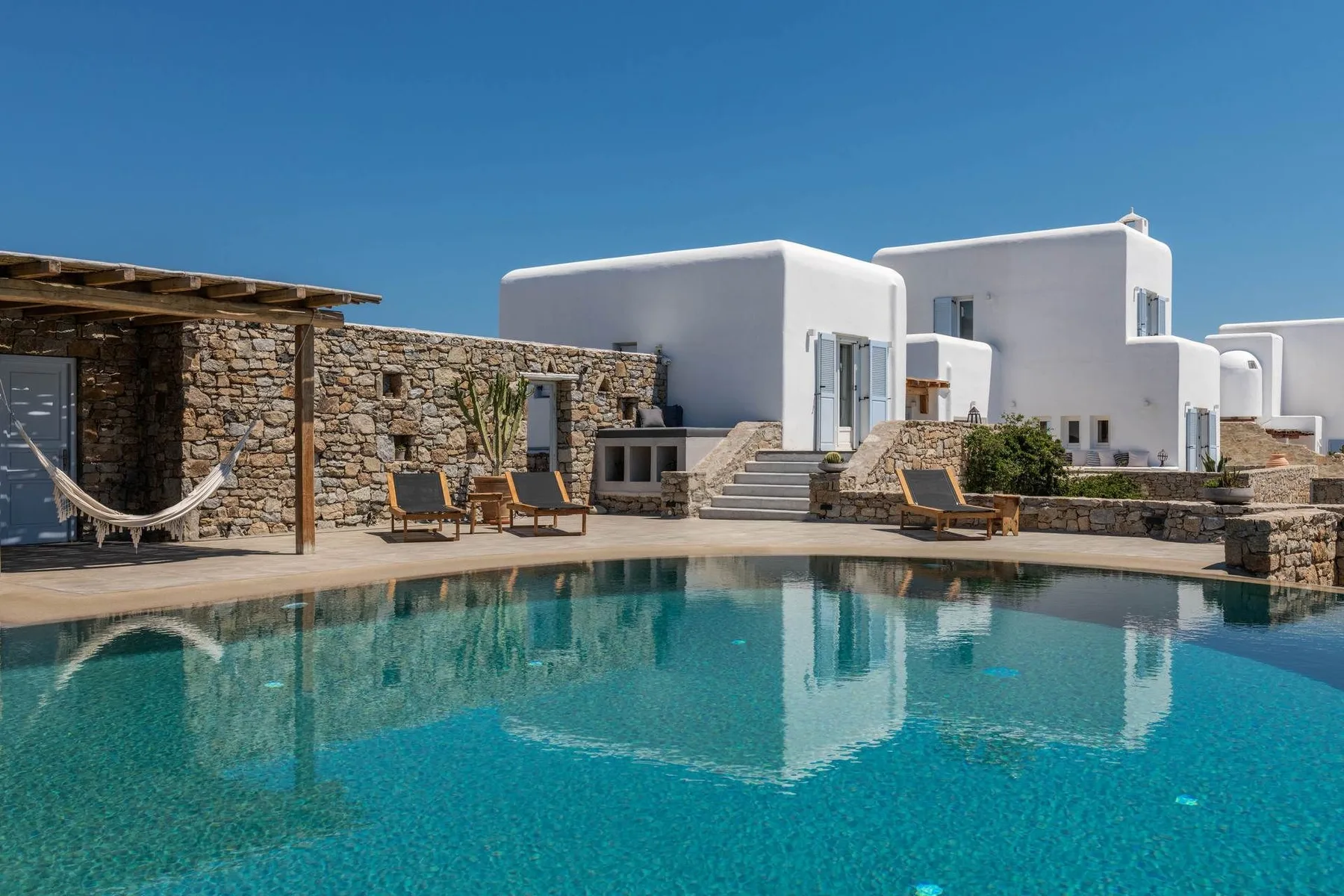 An outdoor pool beside white buildings and a stone patio with seating.