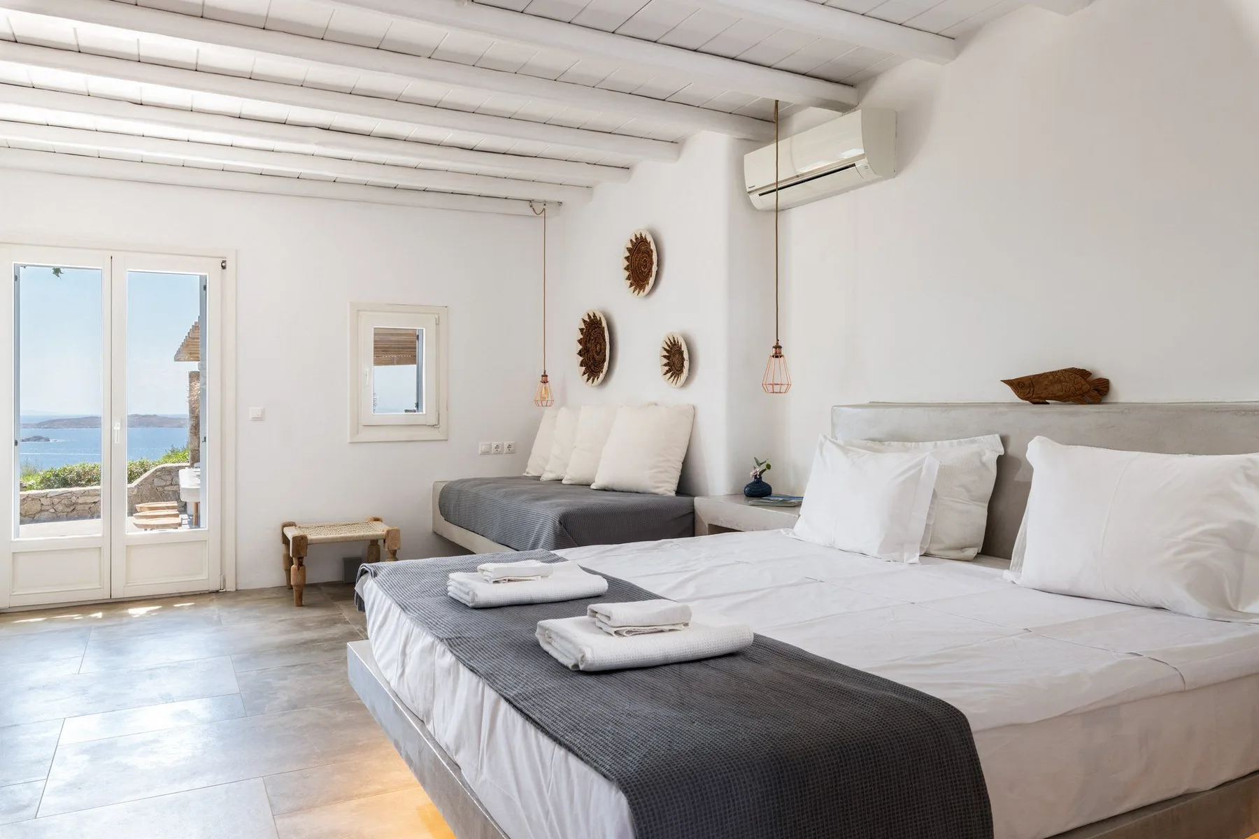 A bright bedroom with two beds, white bedding, and glass doors opening to a balcony.