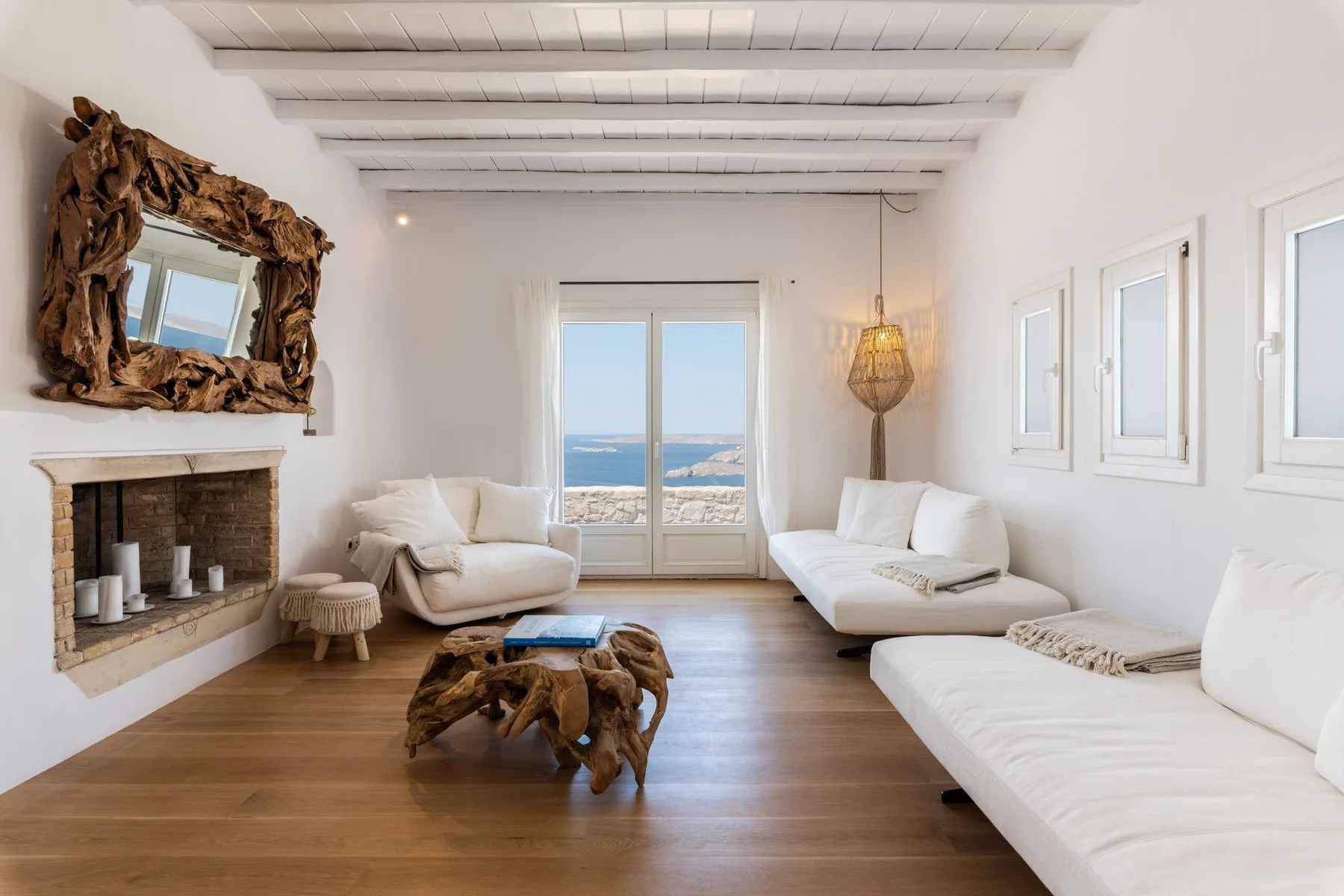 A bright living room with white seating, a fireplace, and windows overlooking the sea.