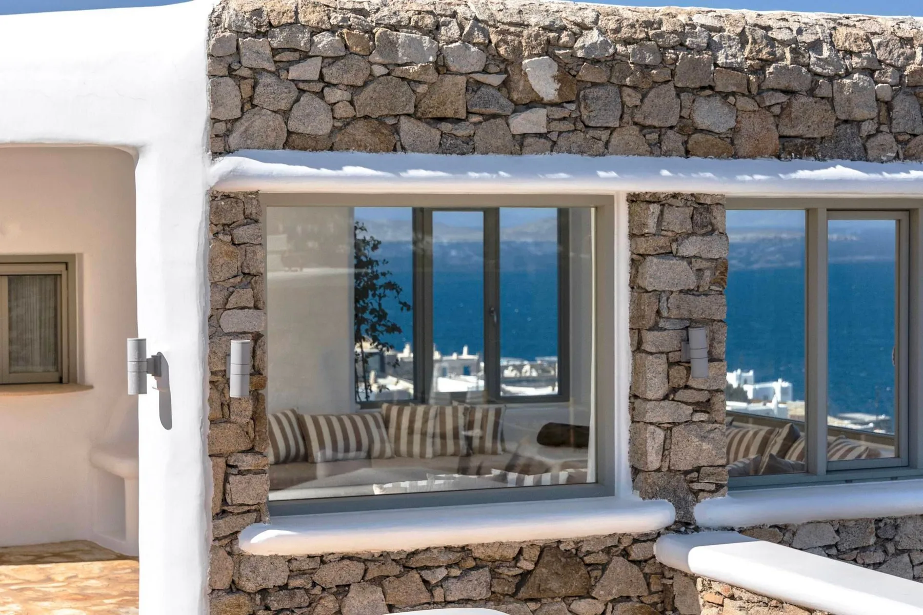 Stone exterior wall with large windows overlooking the sea.
