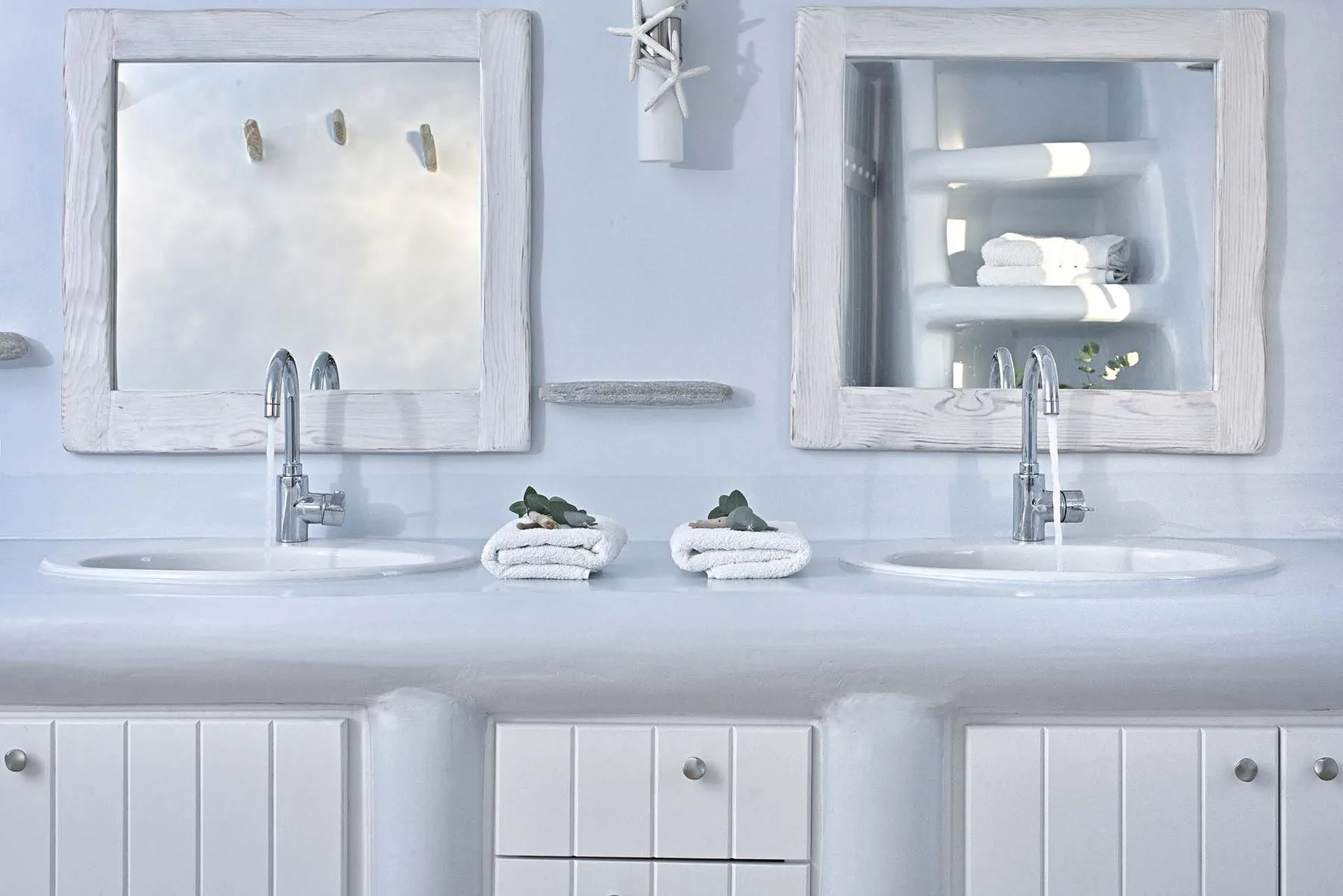 A bright bathroom vanity has two sinks, large mirrors, and folded towels.