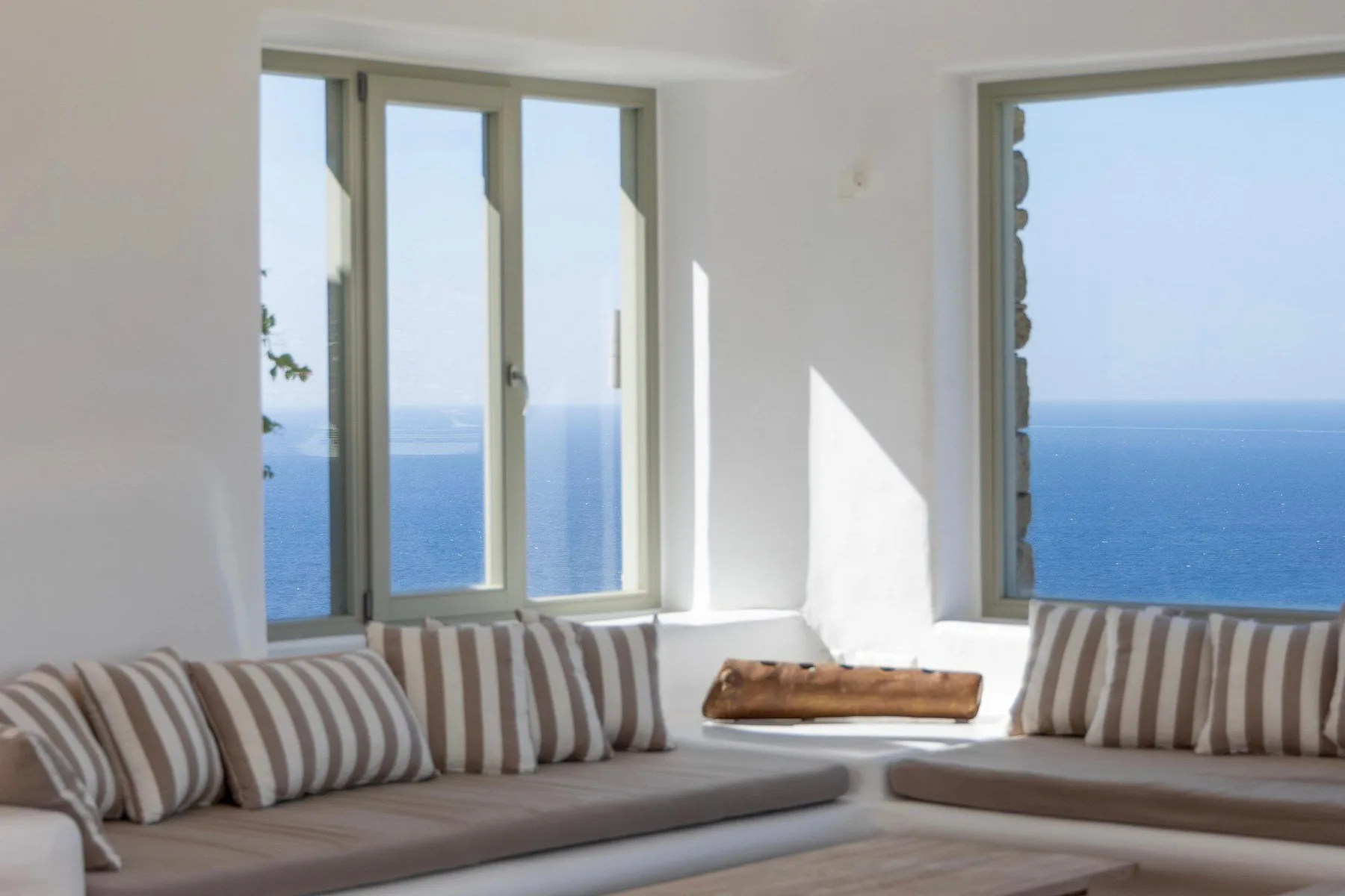 A bright living room with striped seating beside large windows overlooking the sea.