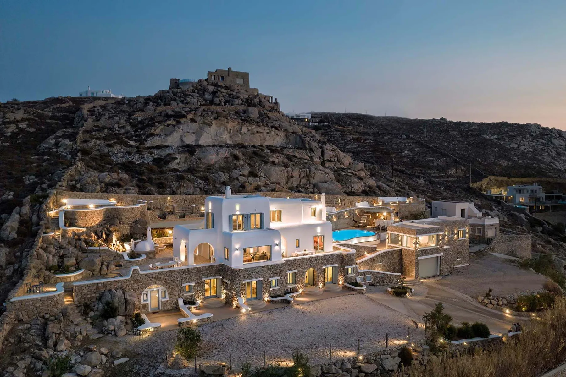 A hillside resort complex with illuminated buildings and a swimming pool at dusk.