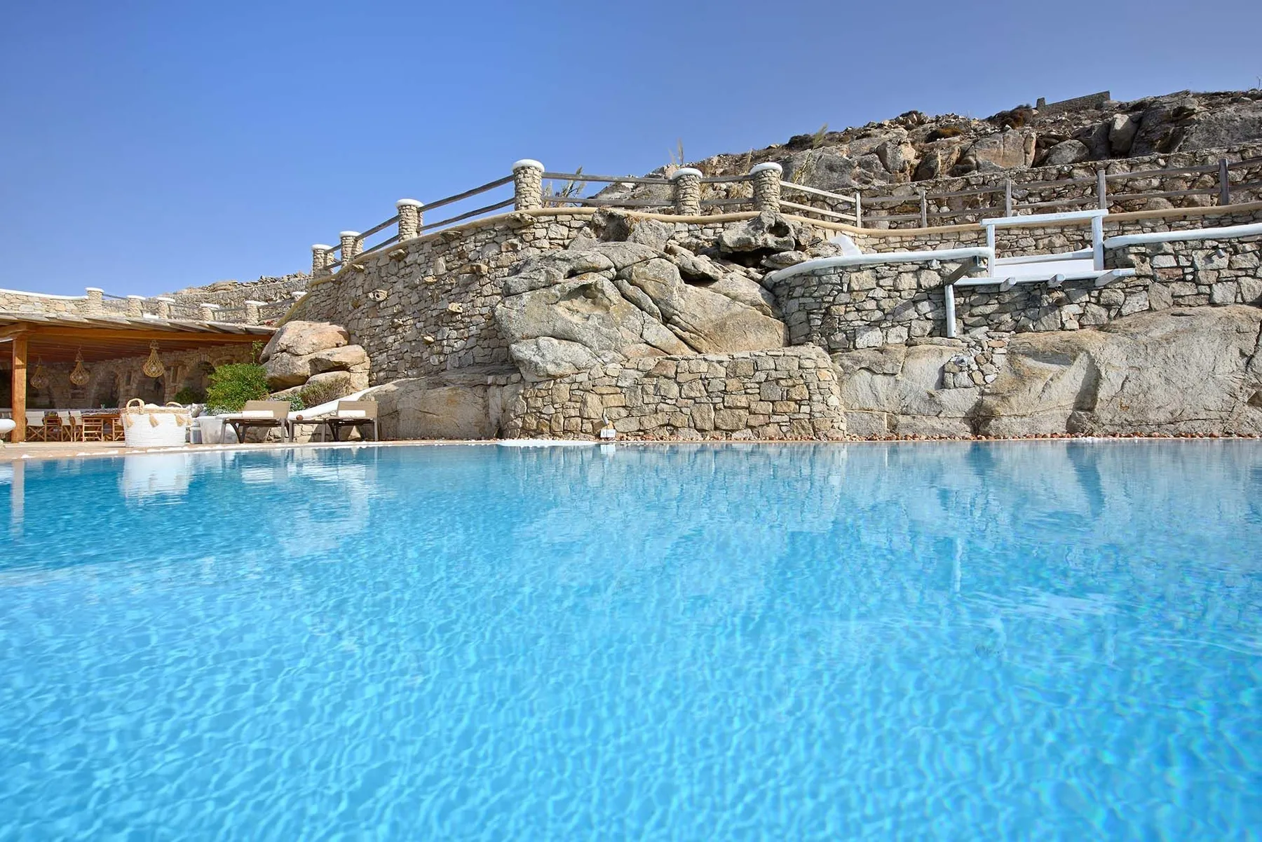 A blue swimming pool sits beside a rocky stone terrace under a clear sky.