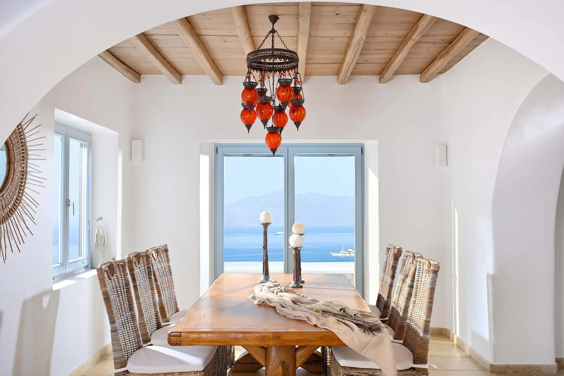 A dining area with a wooden table beneath exposed ceiling beams and a hanging light.