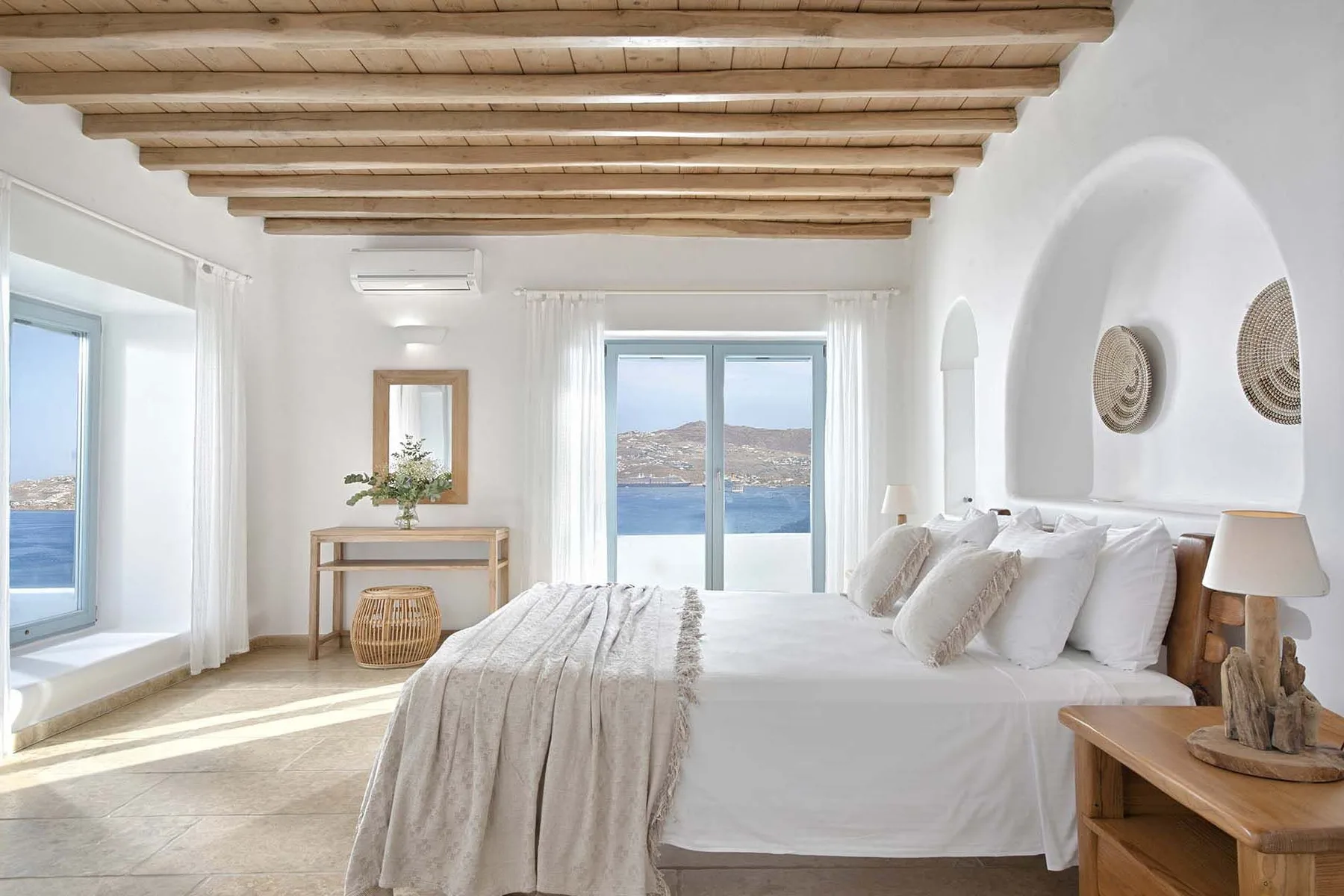 A bright bedroom with a large bed and windows overlooking the water.