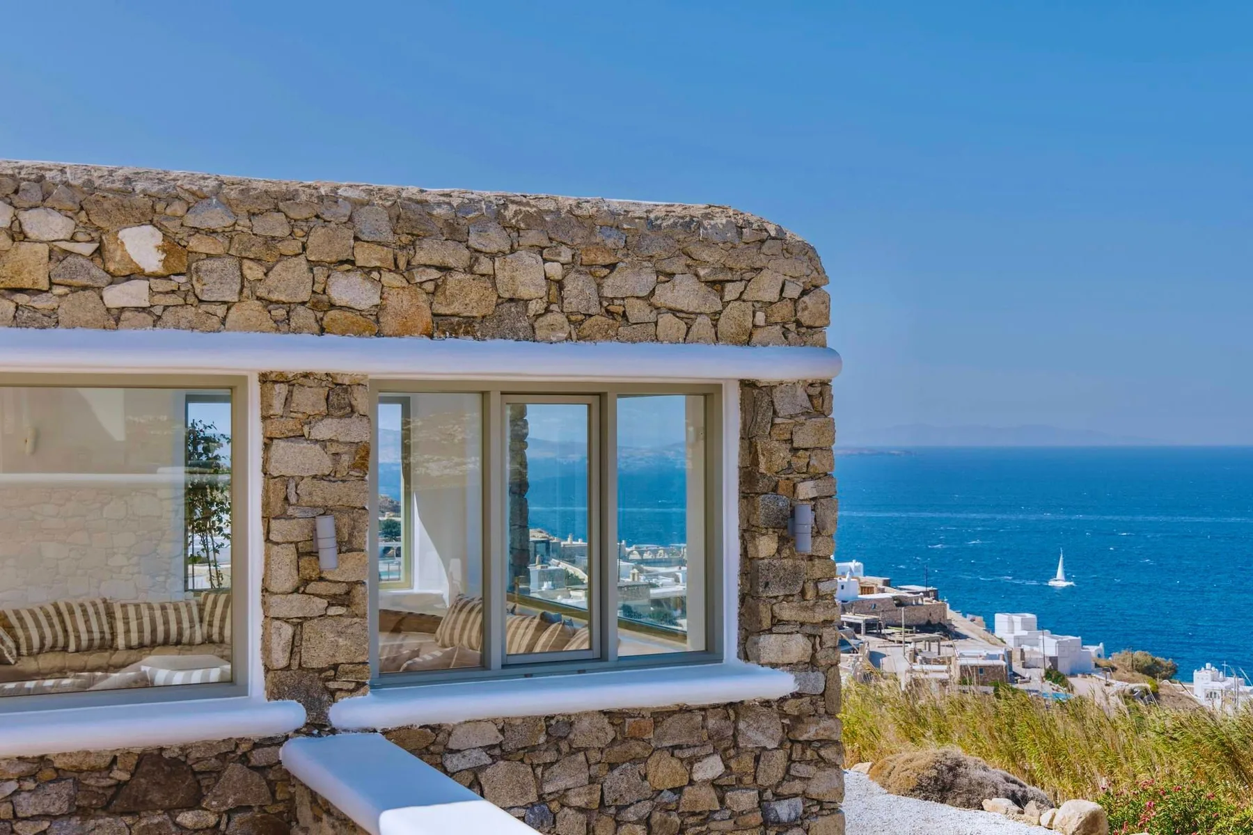 Stone-clad building with large windows overlooks the blue sea.