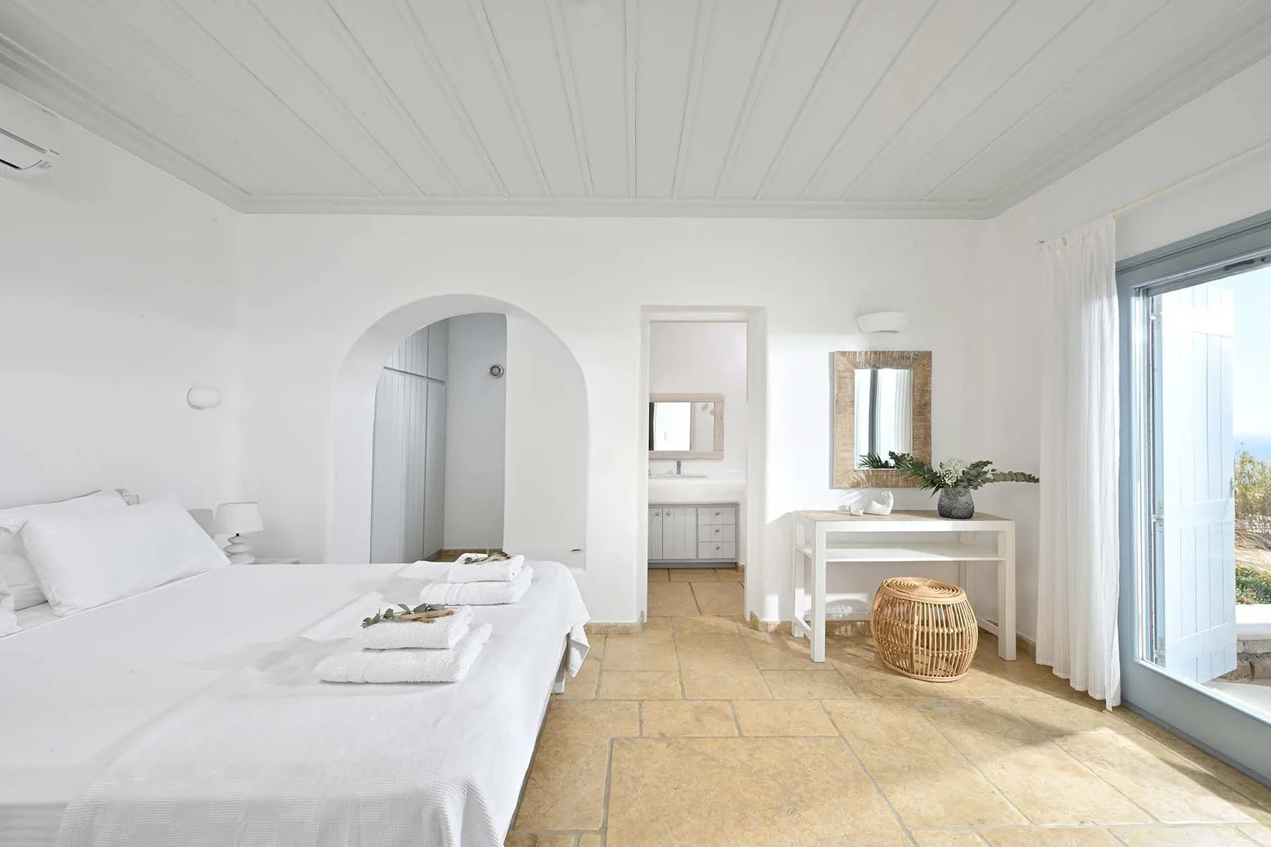 A bright bedroom with a neatly made bed and a vanity beside the window.