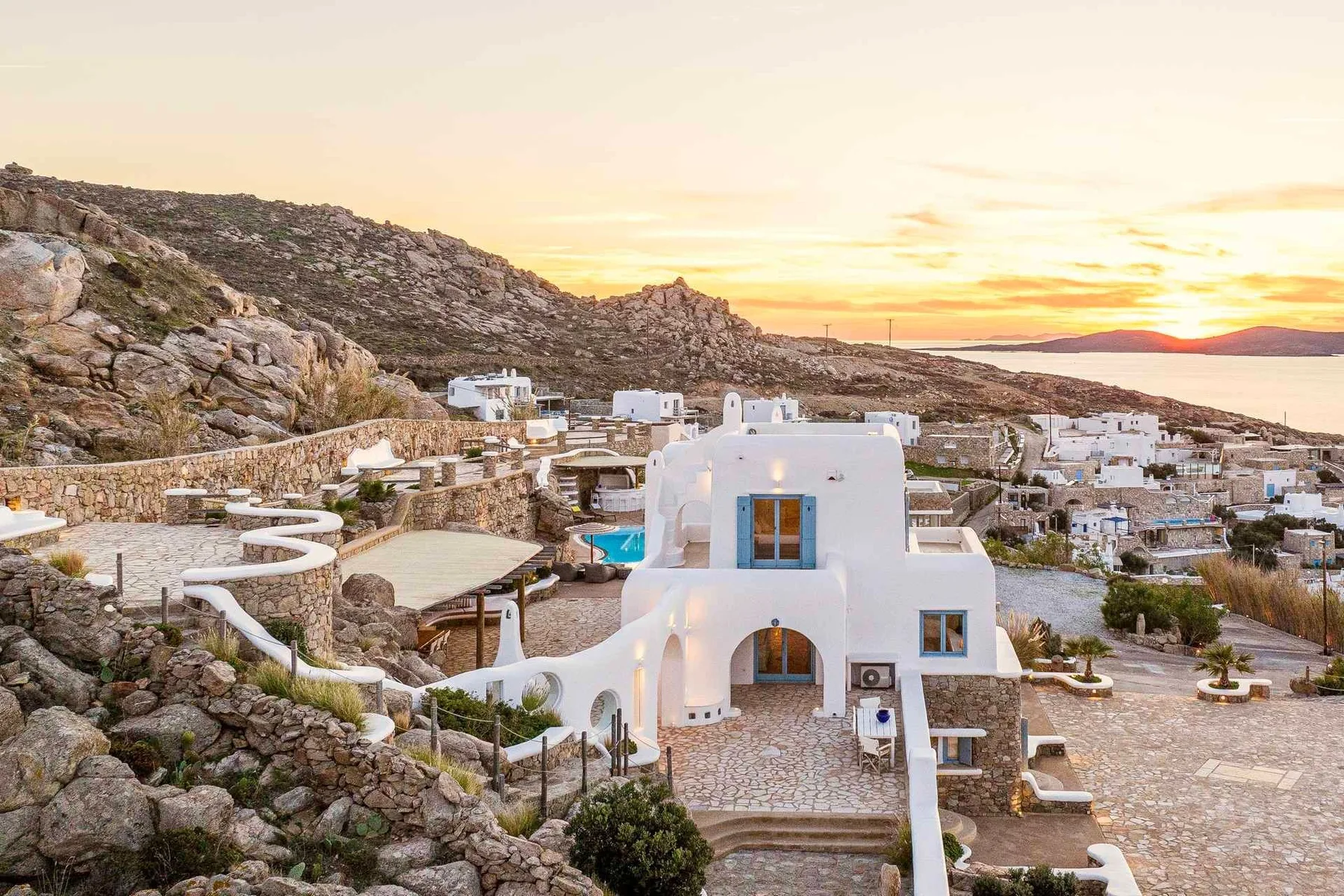 White buildings sit among rocky hillsides beneath a sunset sky.
