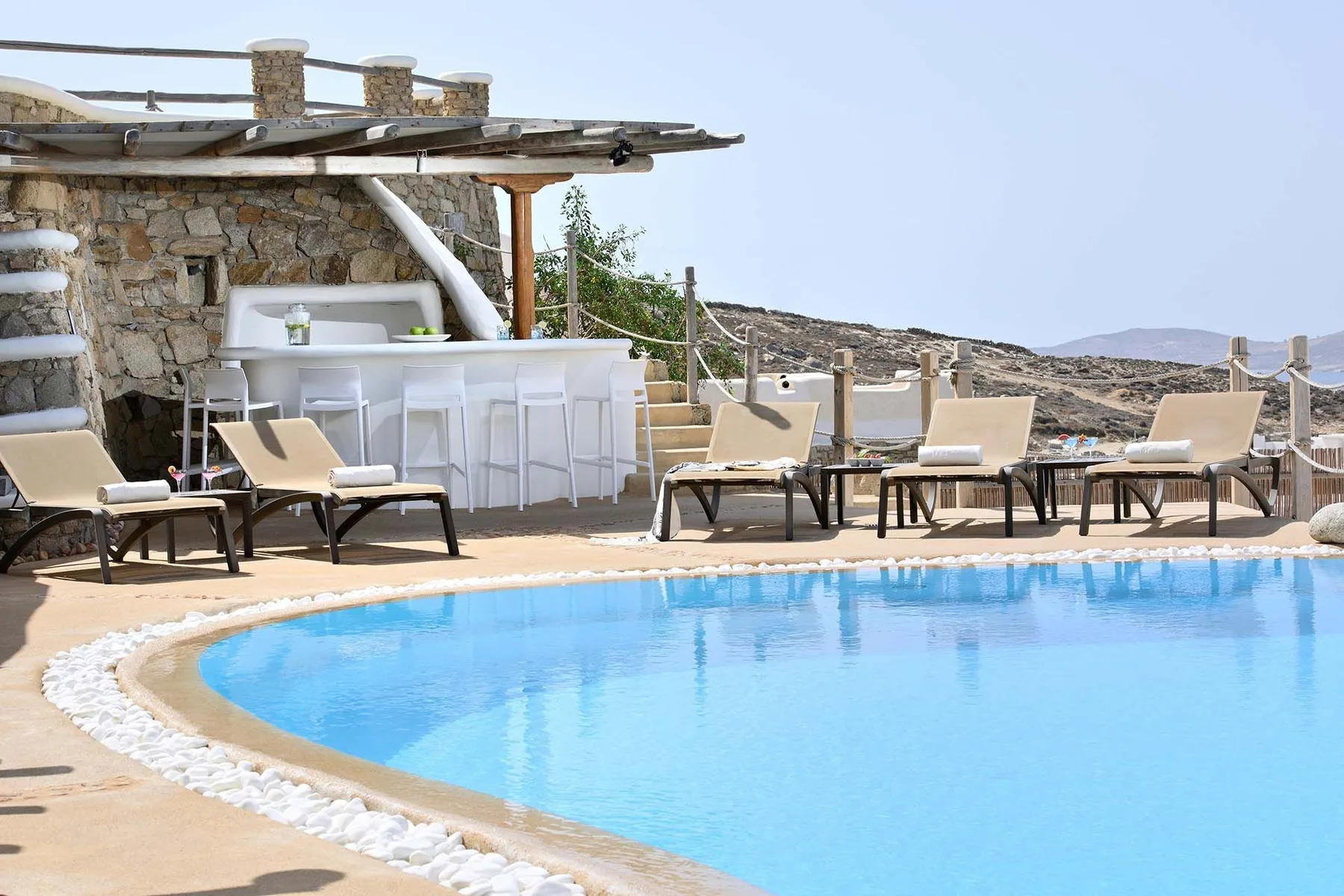 An outdoor swimming pool beside lounge seating and a small bar.