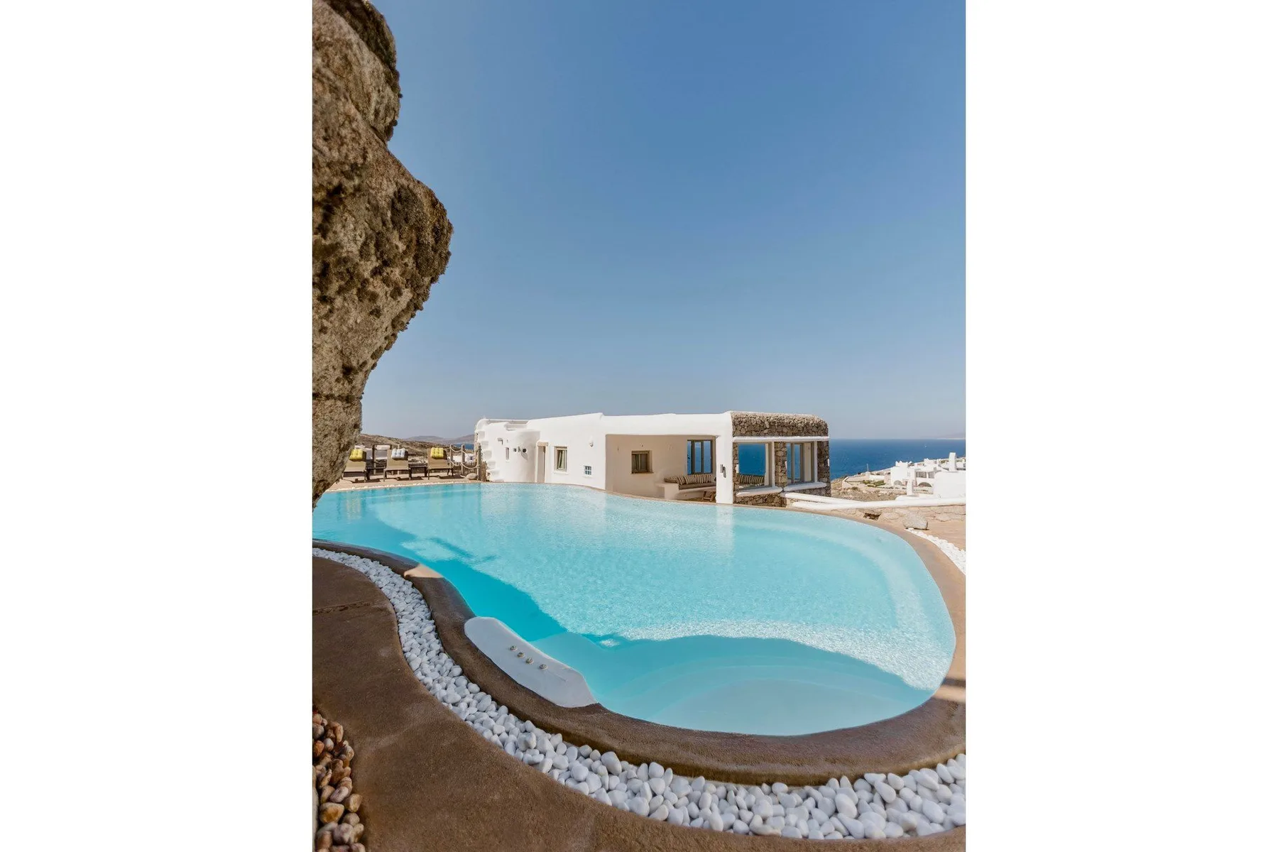A curved swimming pool sits beside a white building overlooking the sea.