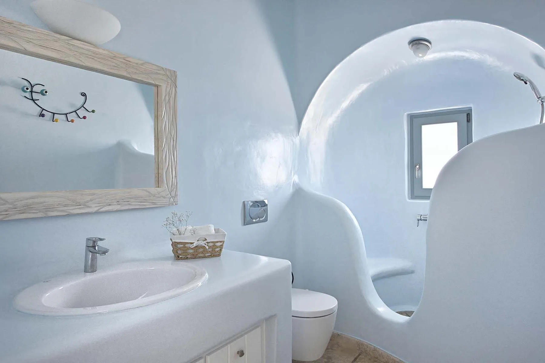 A curved white bathroom with a sink, mirror, and toilet.