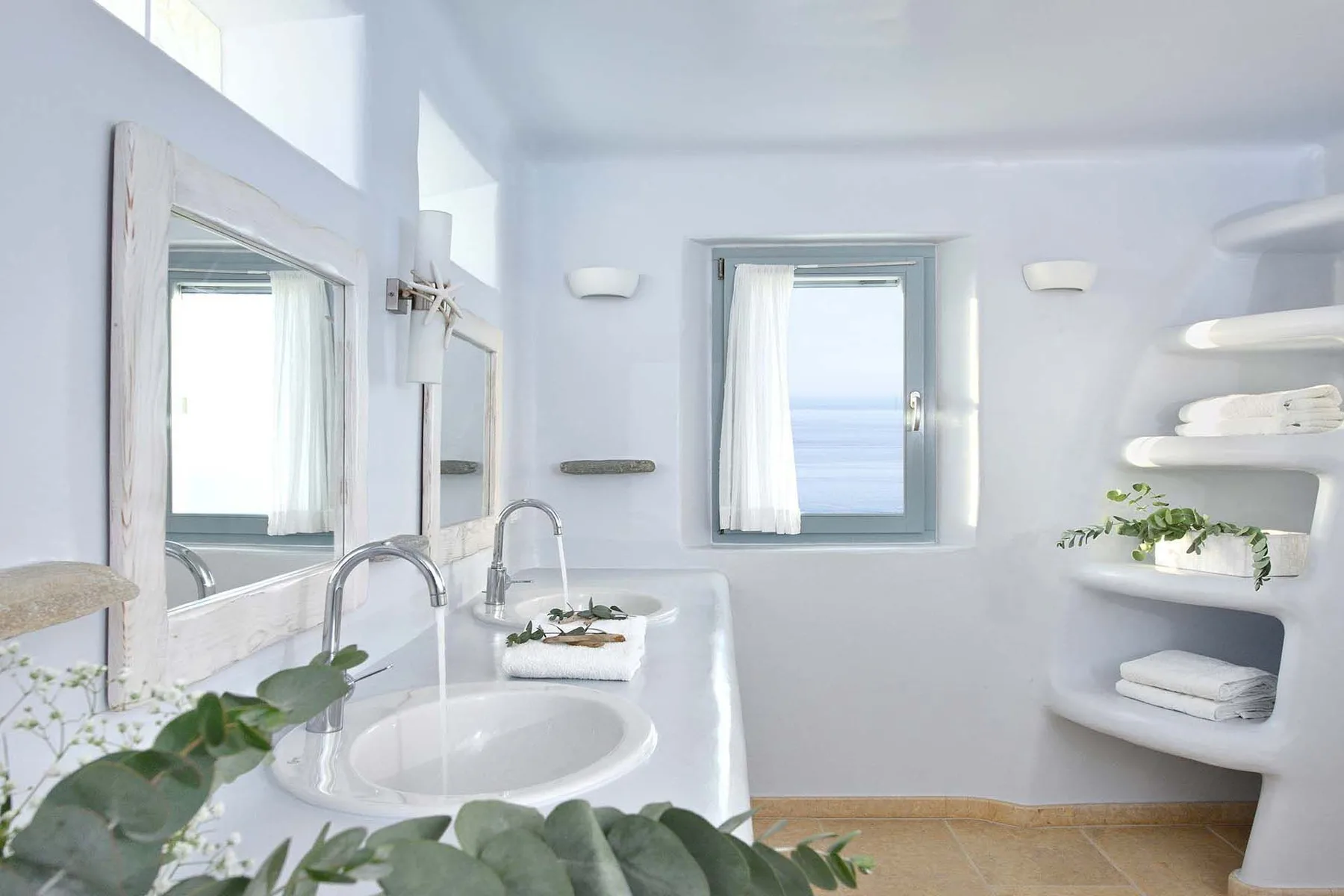 A bright bathroom with a sink, mirror, and window overlooking the sea.