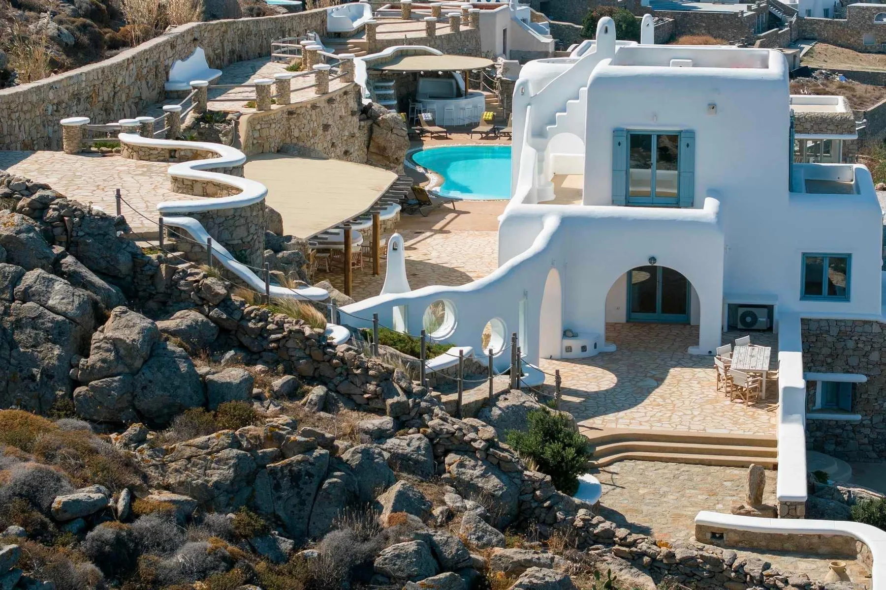 A white building beside a bright blue pool, surrounded by stone terraces.
