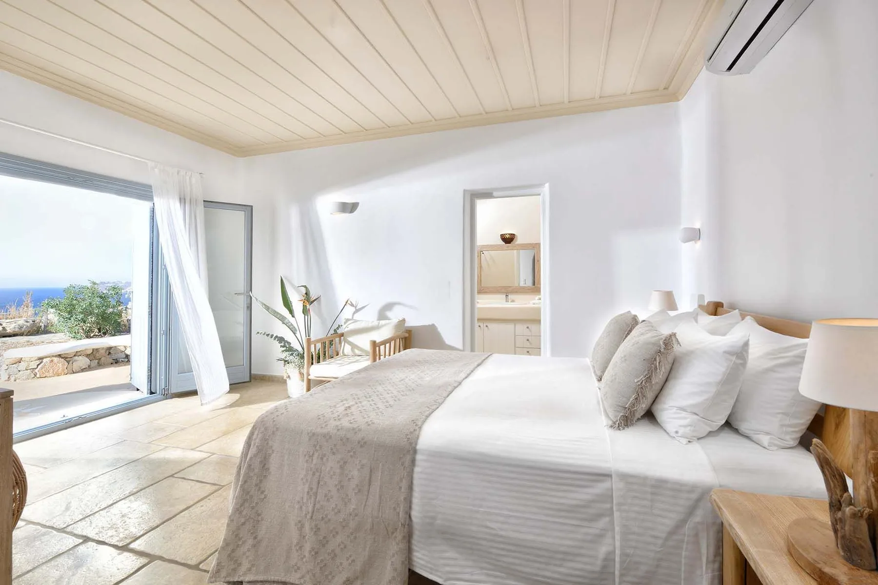 A bright bedroom with a bed beside open sliding glass doors.