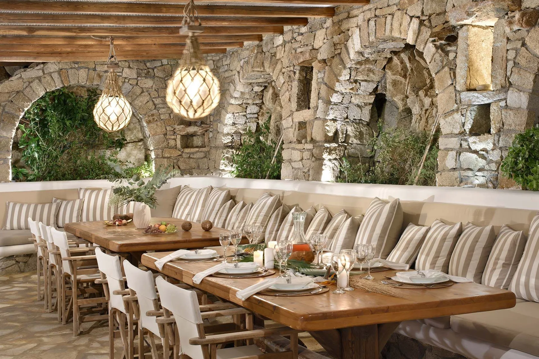 A dining area with long wooden tables, cushioned seating, and stone arches.