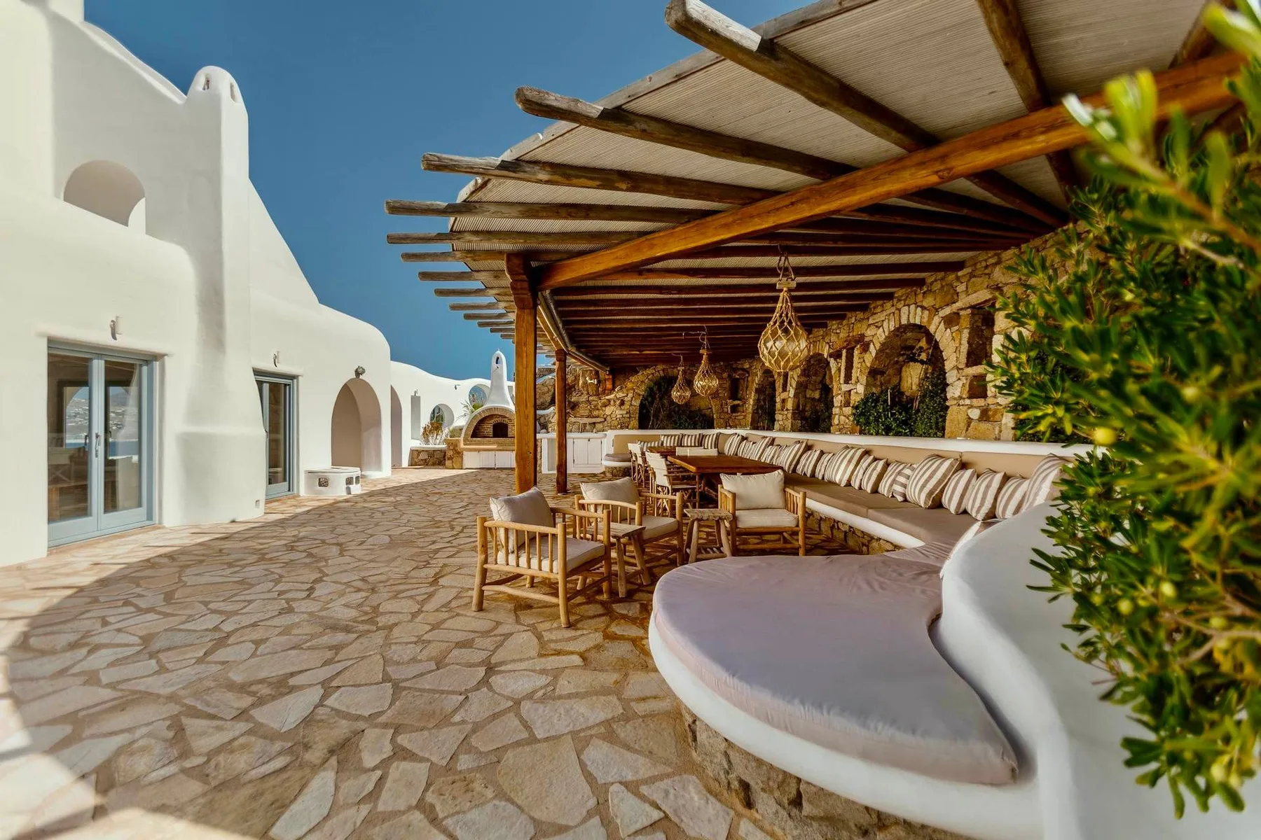 A shaded outdoor seating area beside white buildings, with a stone-paved courtyard.