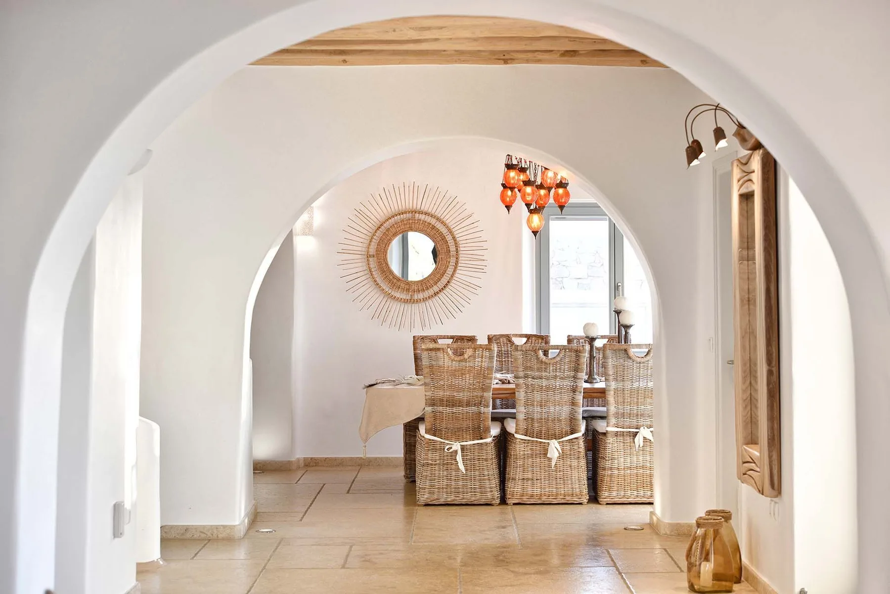 A dining area with woven seating sits beyond a rounded archway.
