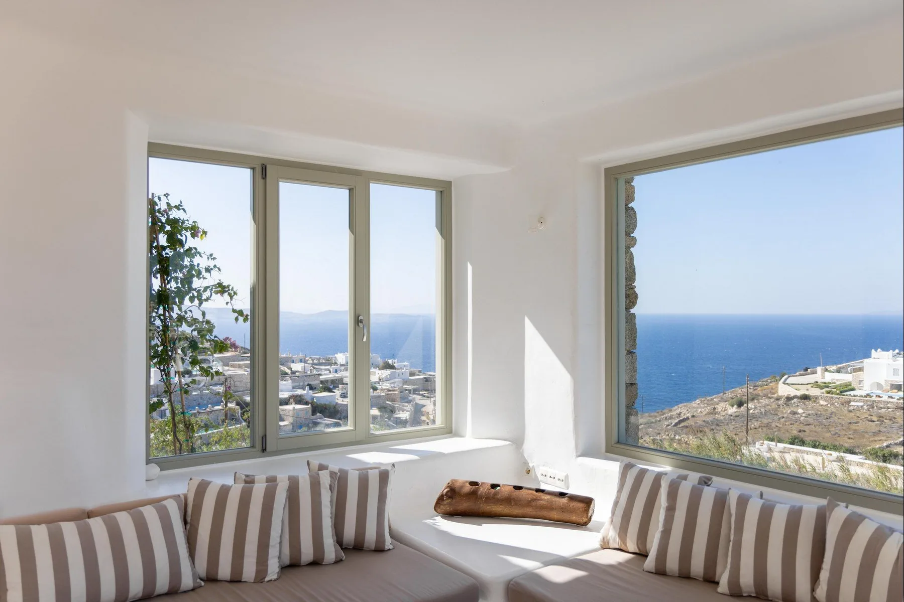 A bright living room with striped cushions beside large windows overlooking the sea.