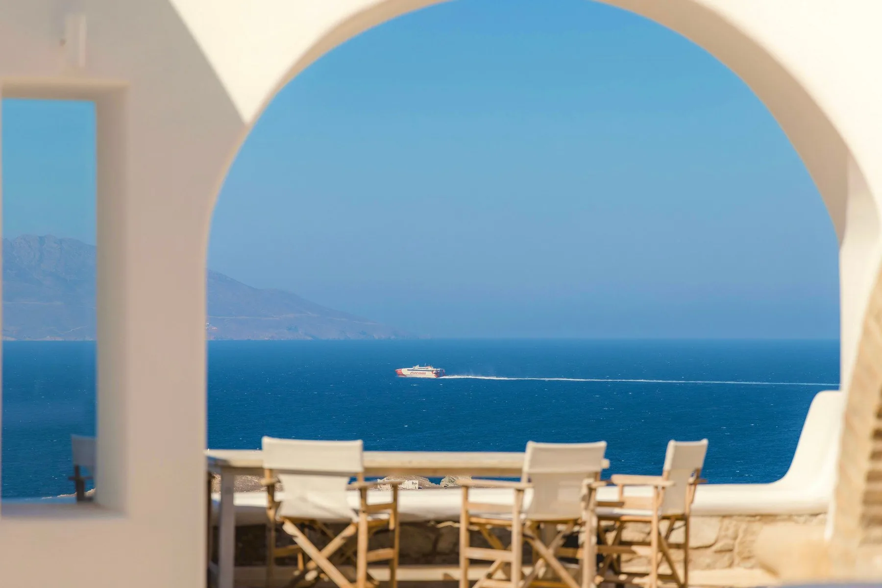 A seaside dining area with chairs and a table beneath a large arch.