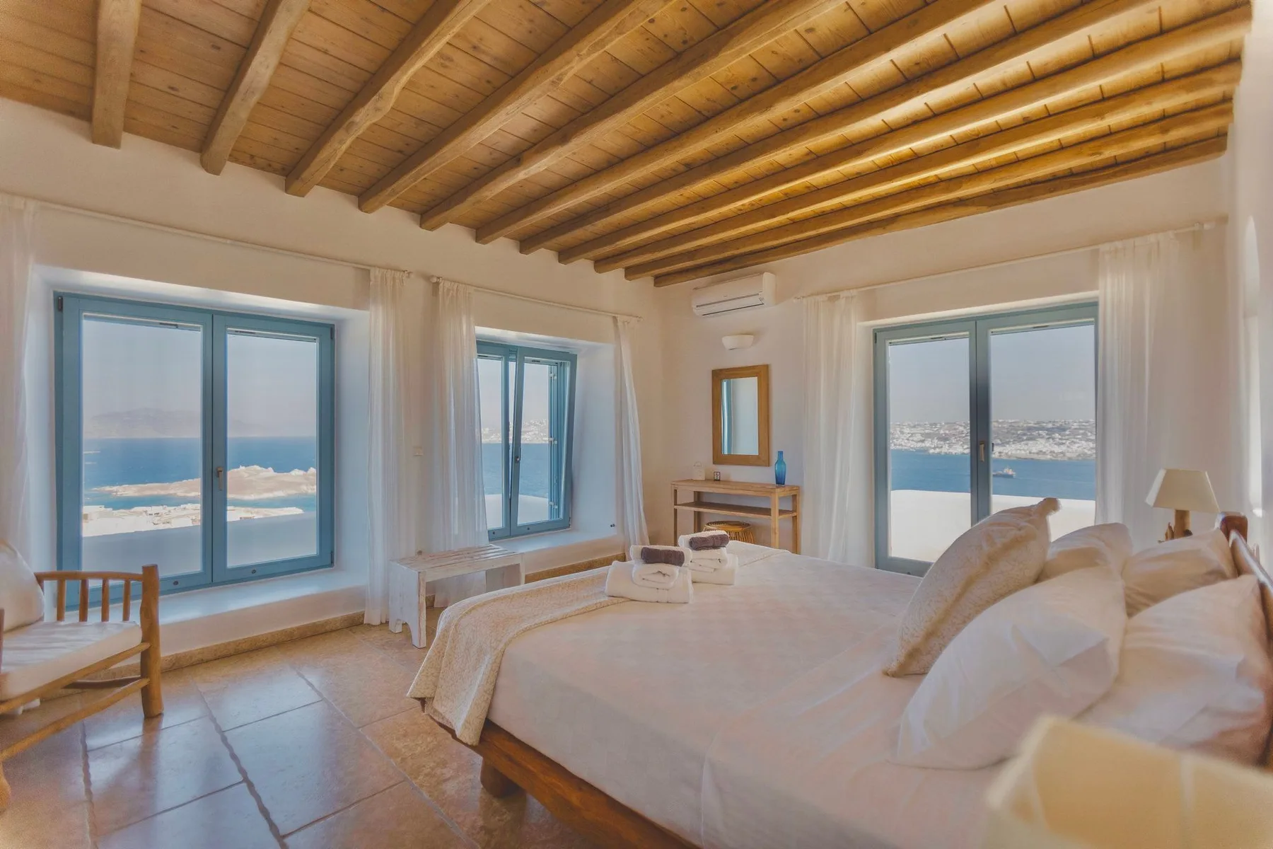 A bright bedroom with a large bed and windows overlooking the sea.