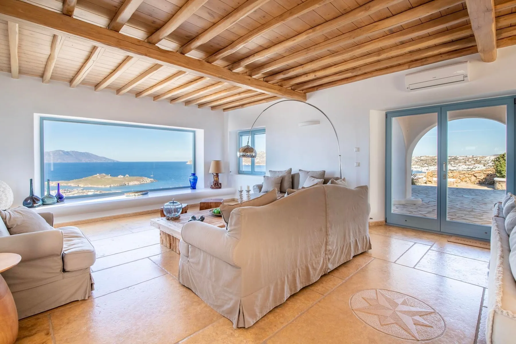 A living room with beige seating and wide windows overlooking the sea.