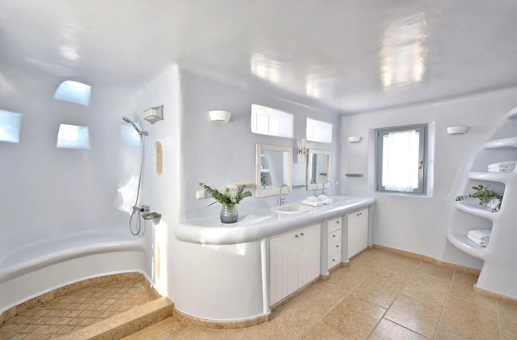A bright bathroom with a curved vanity, sinks, and a shower.