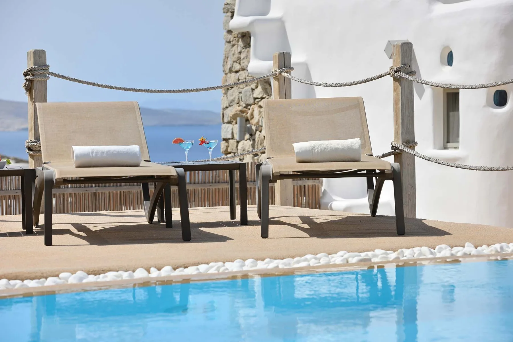 Two loungers sit beside a swimming pool on a terrace overlooking the sea.