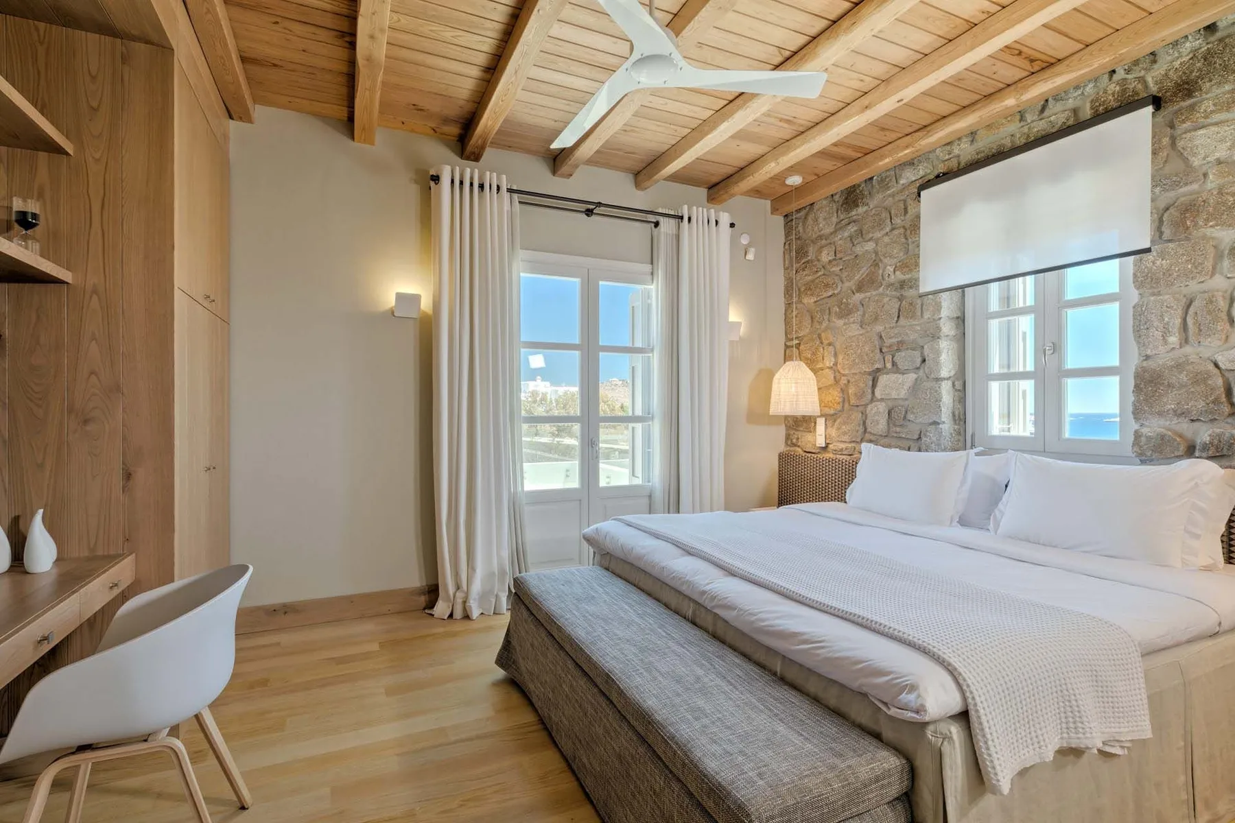 A bedroom with a bed beneath a wooden ceiling and windows.