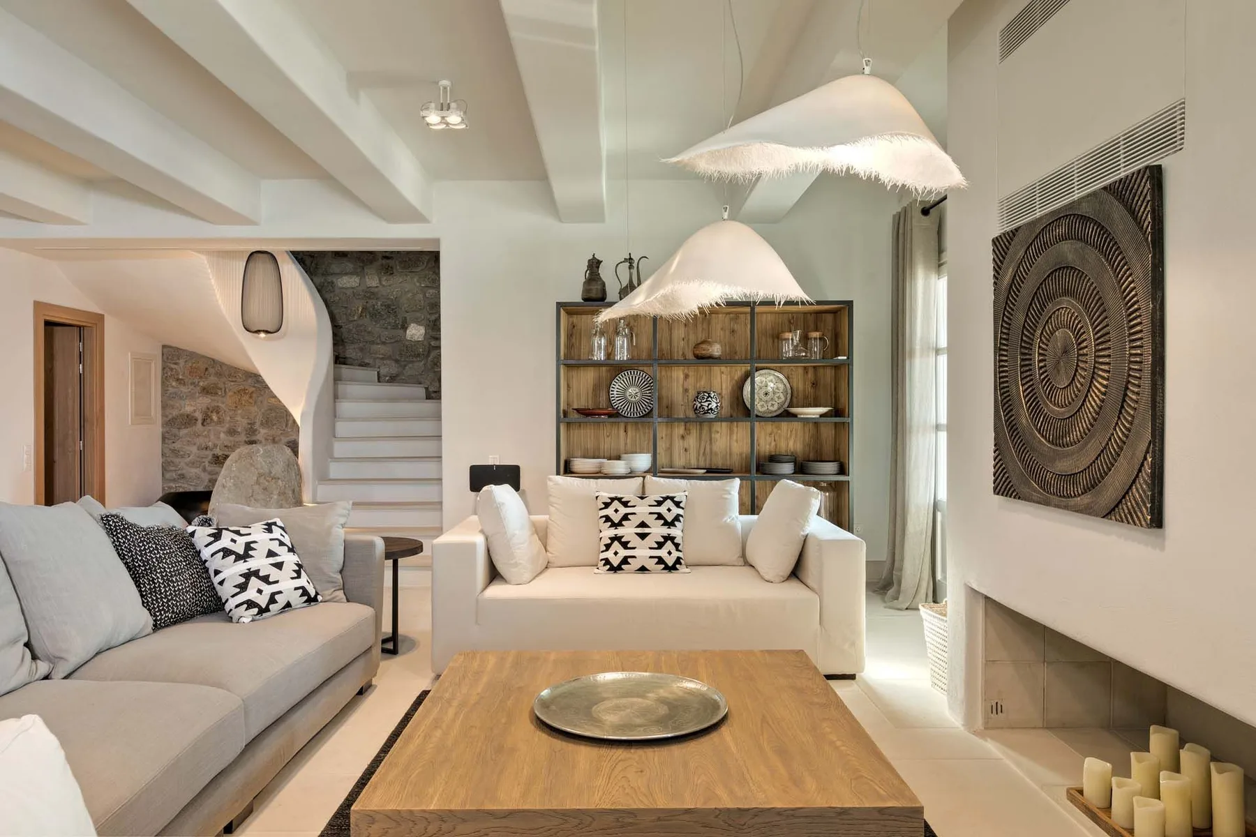 A bright living room with pale seating, a wooden coffee table, and a display shelf.