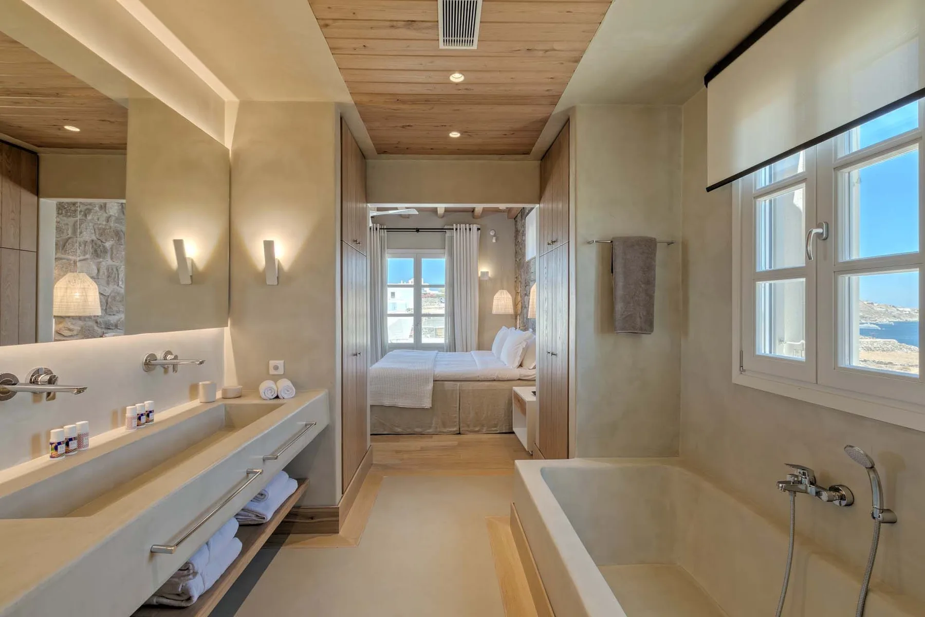 A bright bathroom with a bathtub, double sinks, and a view into a bedroom.