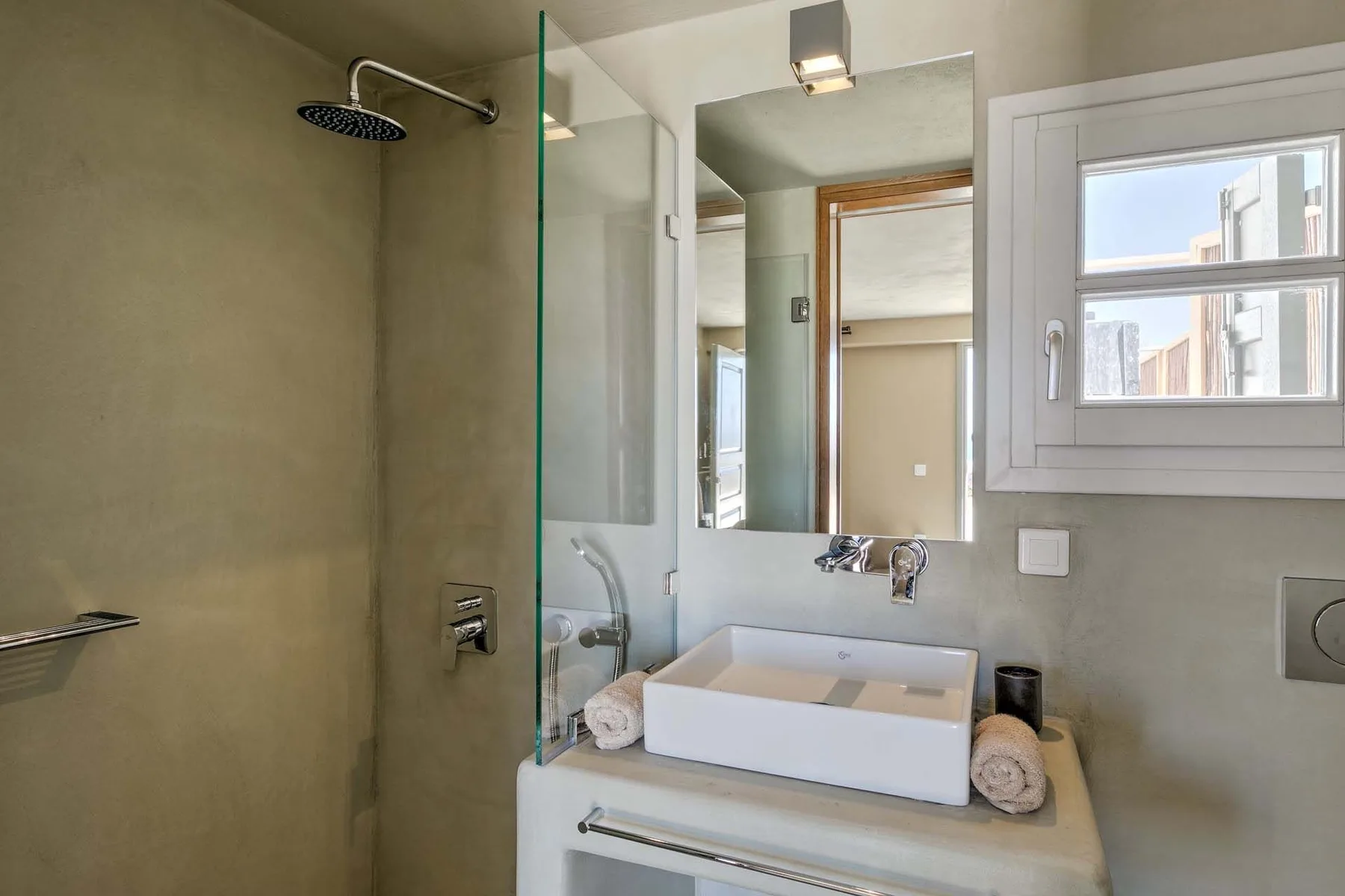 A bathroom with a glass shower, sink, and window.
