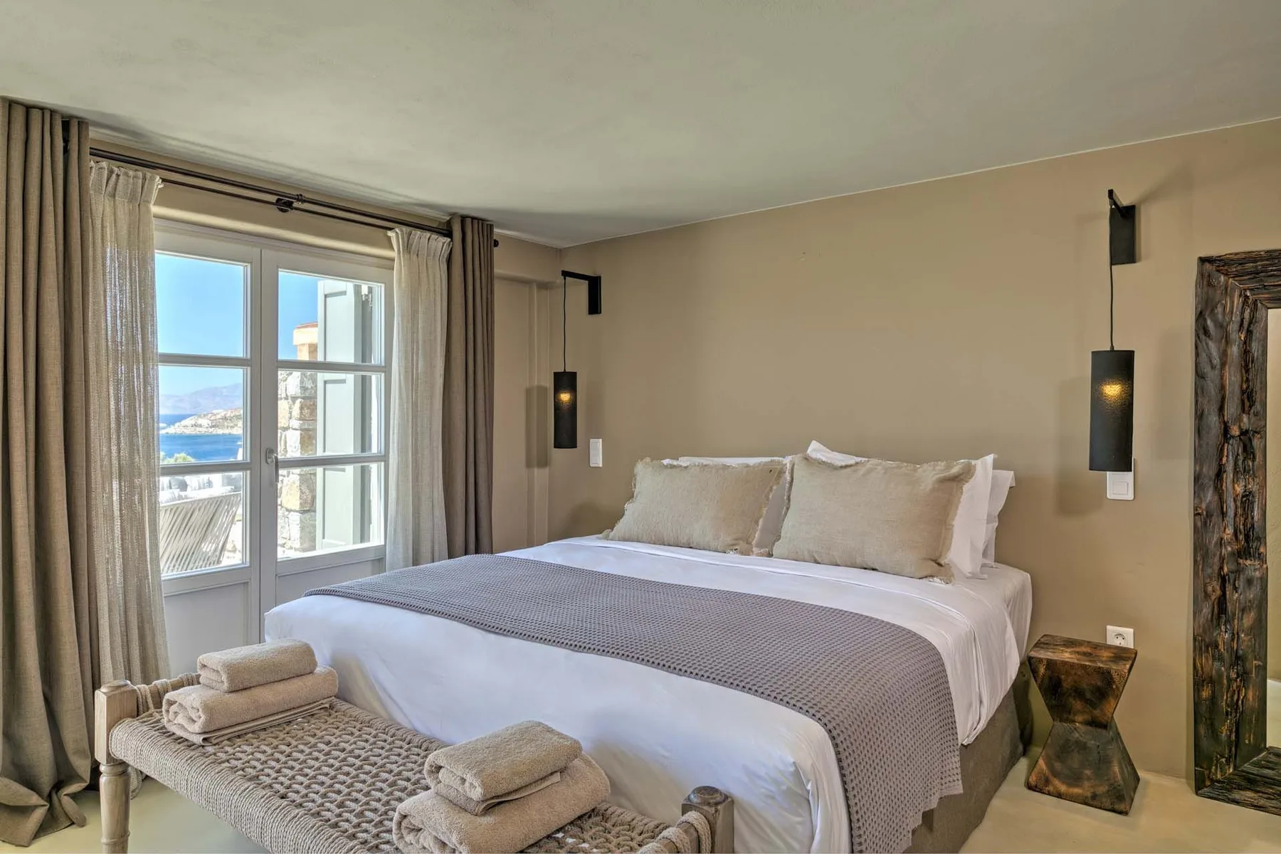 A bedroom with a neatly made bed beside a glass door opening onto a balcony.