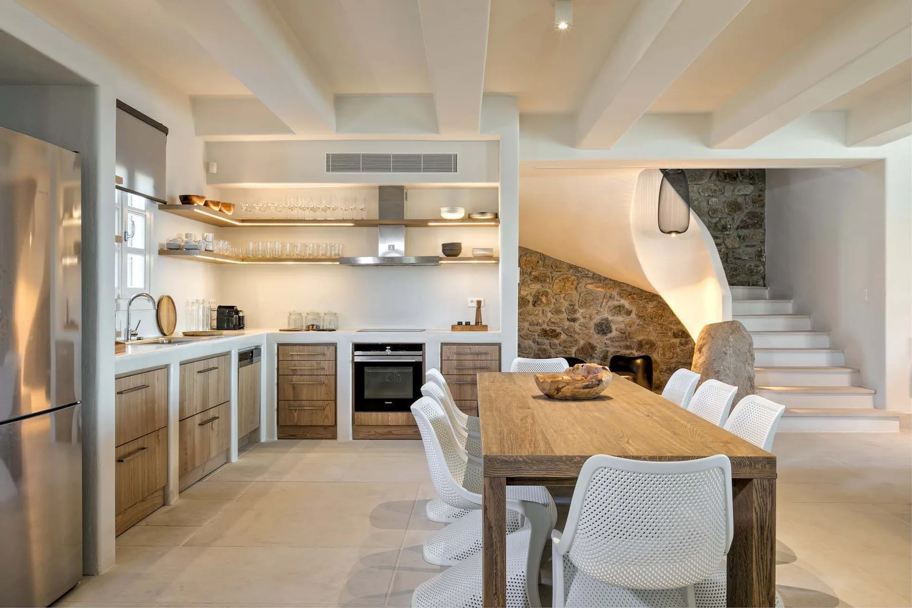 A bright open-plan kitchen and dining area with a wooden table and staircase.