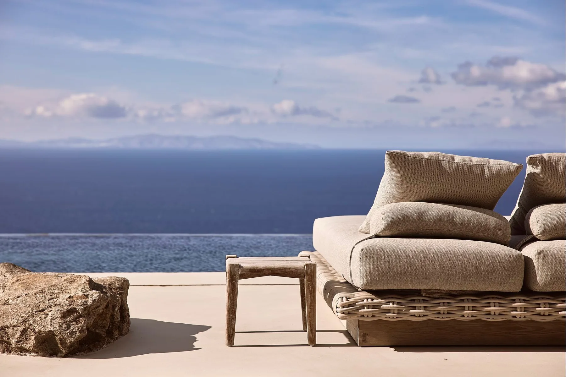 Outdoor seating faces a calm sea beneath a partly cloudy sky.