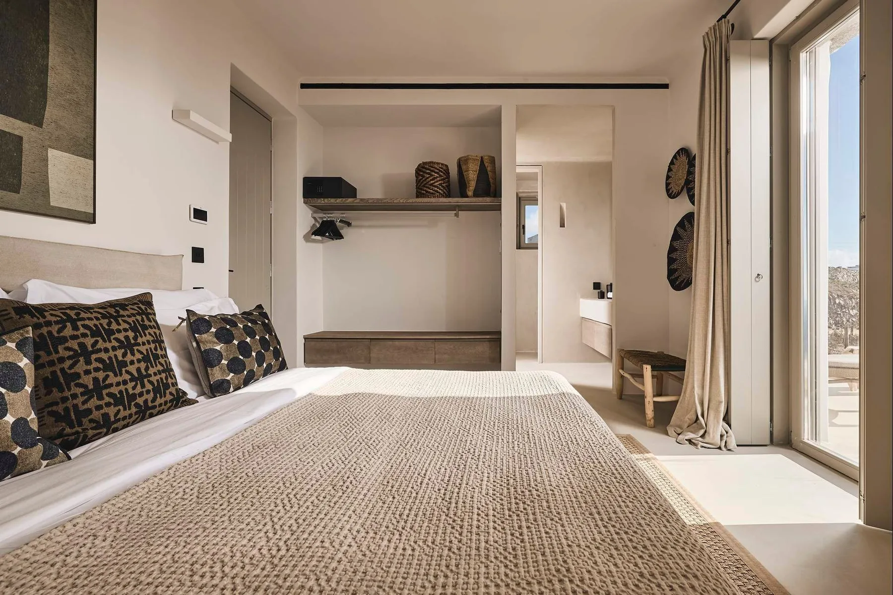 A bedroom with a bed, patterned pillows, and large glass doors.