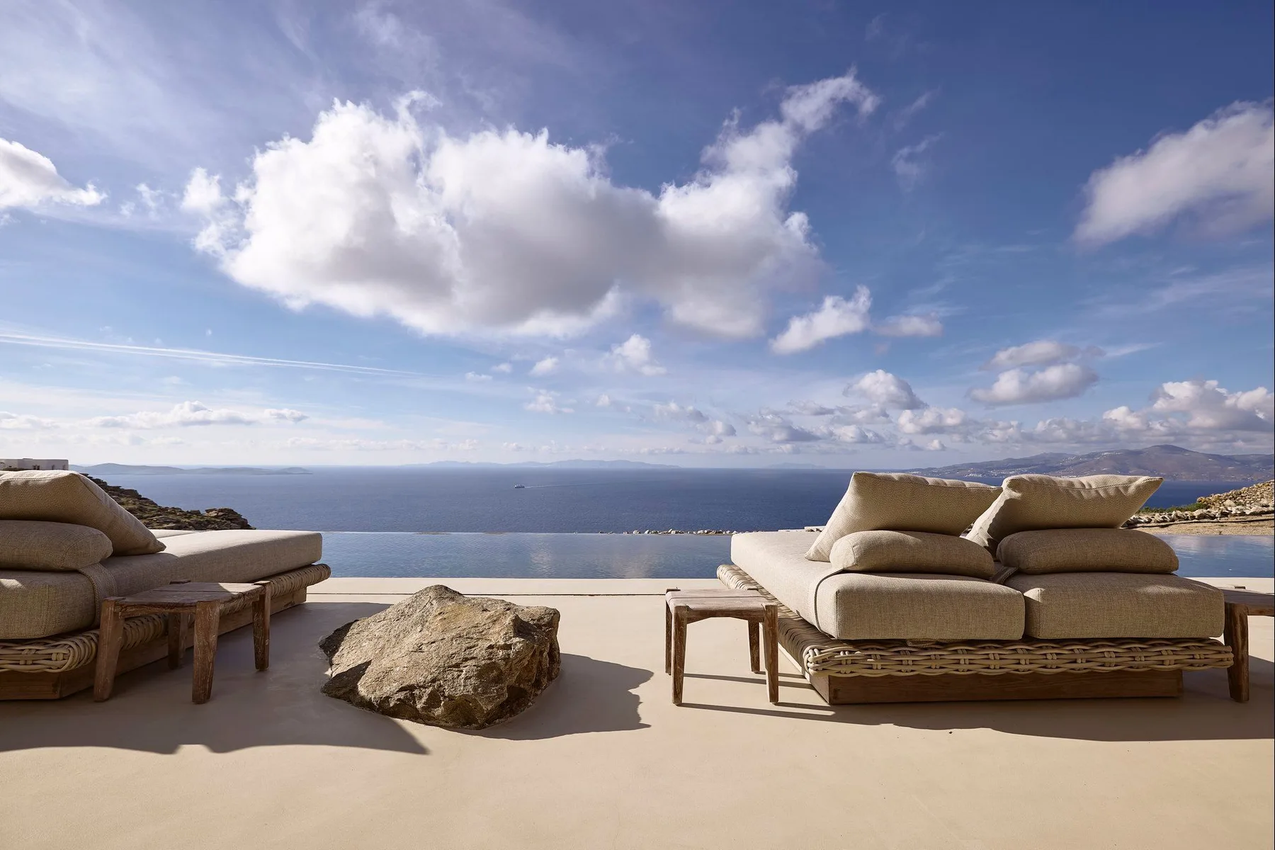 An outdoor seating area overlooks the sea beneath a partly cloudy sky.