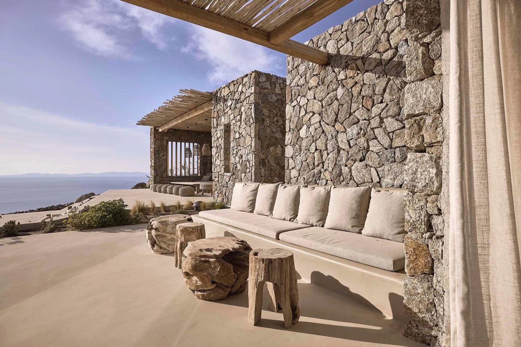 An outdoor patio with cushioned seating beside a stone wall overlooks the water.
