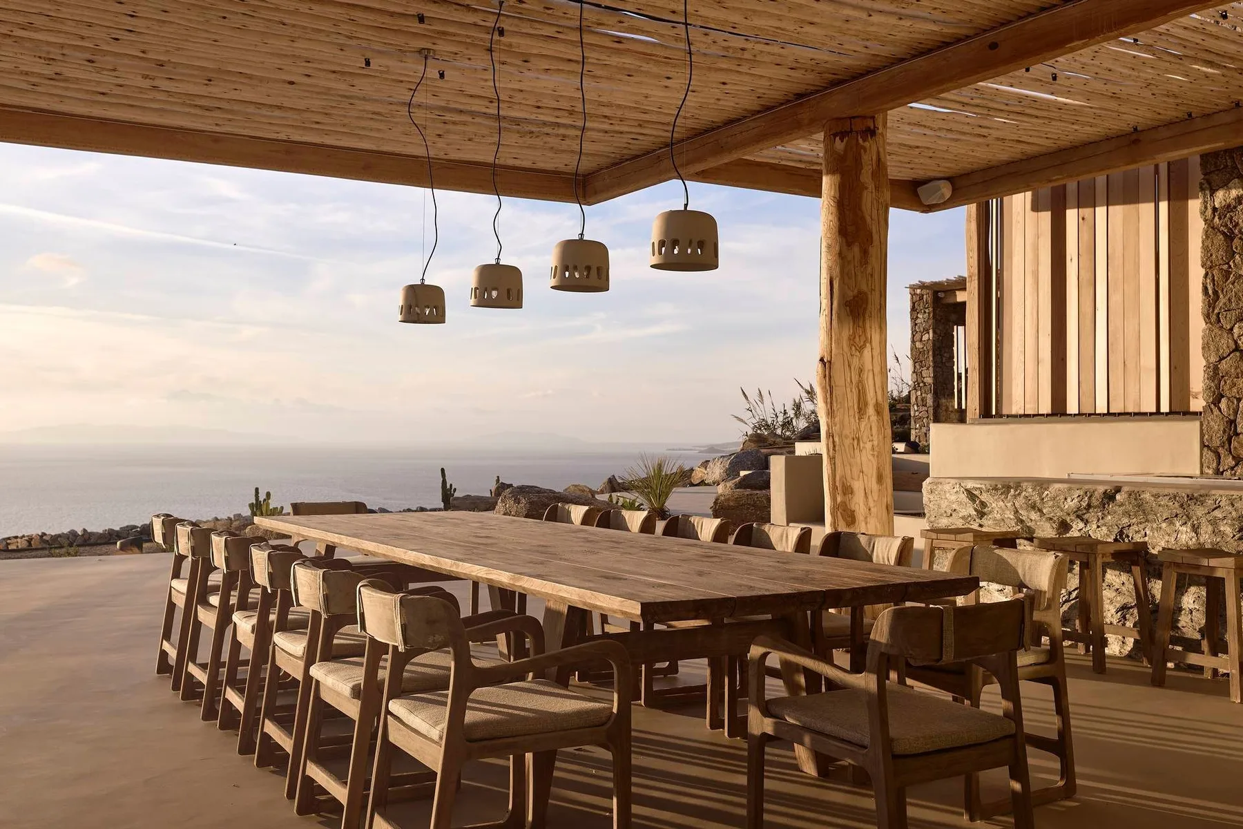 An outdoor dining area with a long wooden table and views of the sea.
