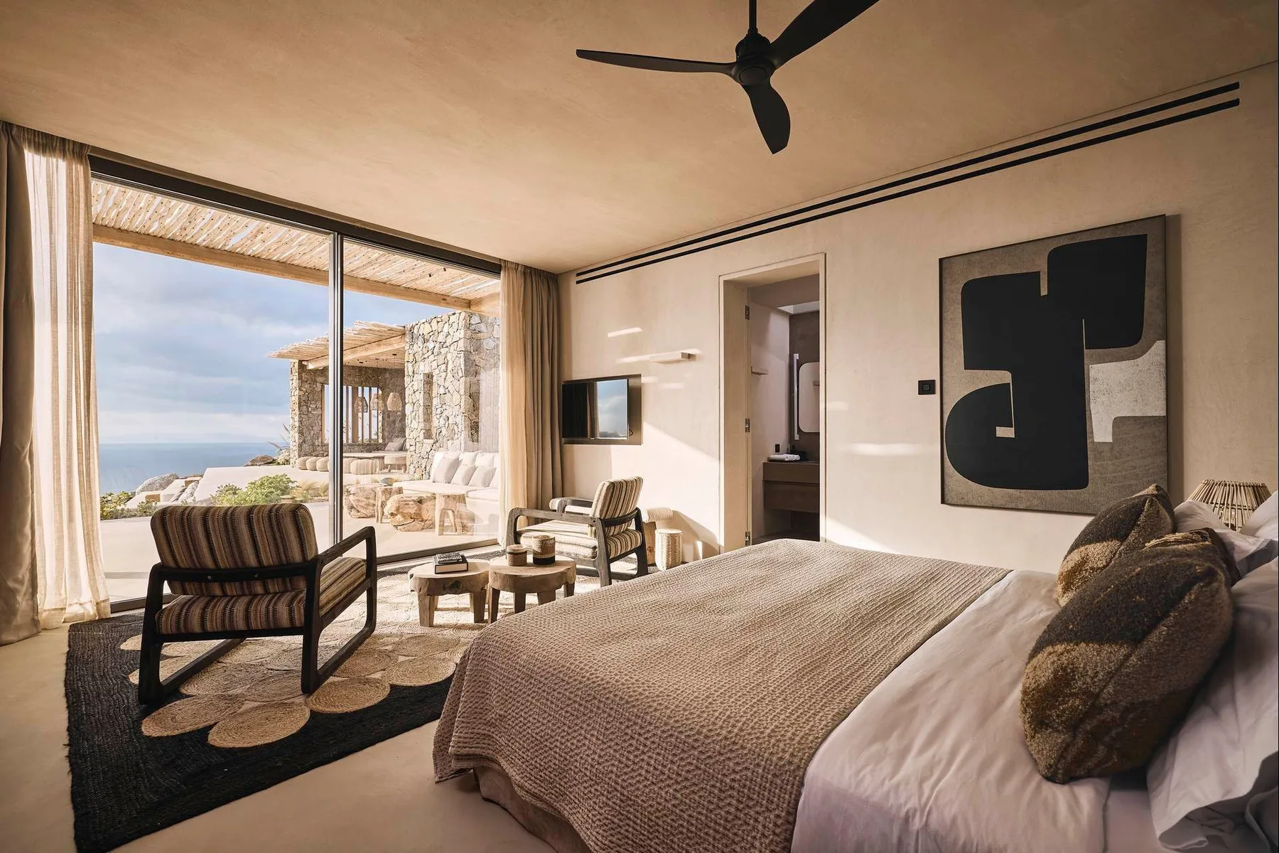 A bedroom with a large bed, seating area, and sliding glass doors opening to a patio.